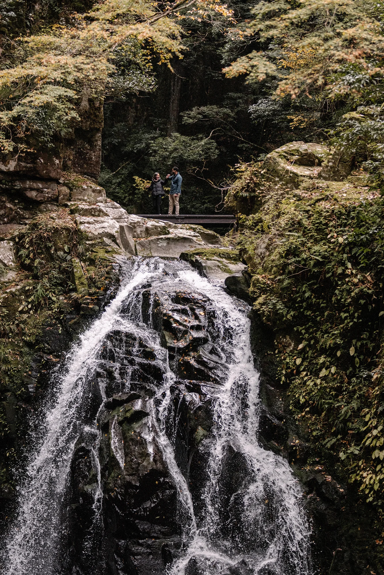 A couple on a footbridge above a waterfall at Akame 48 Falls.