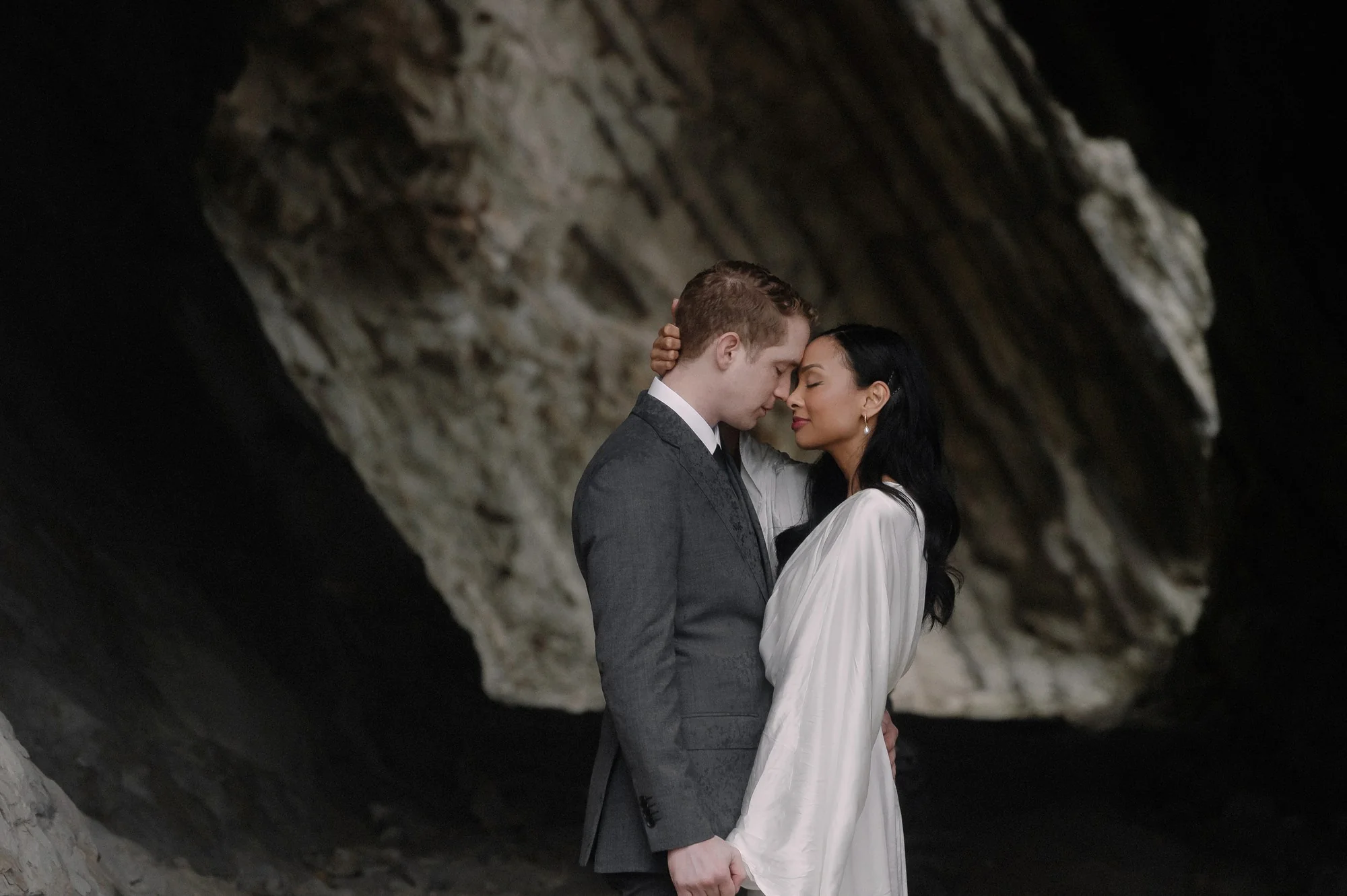 A couple kiss inside a sea cave on the Miura coast, the rock arching above them.
