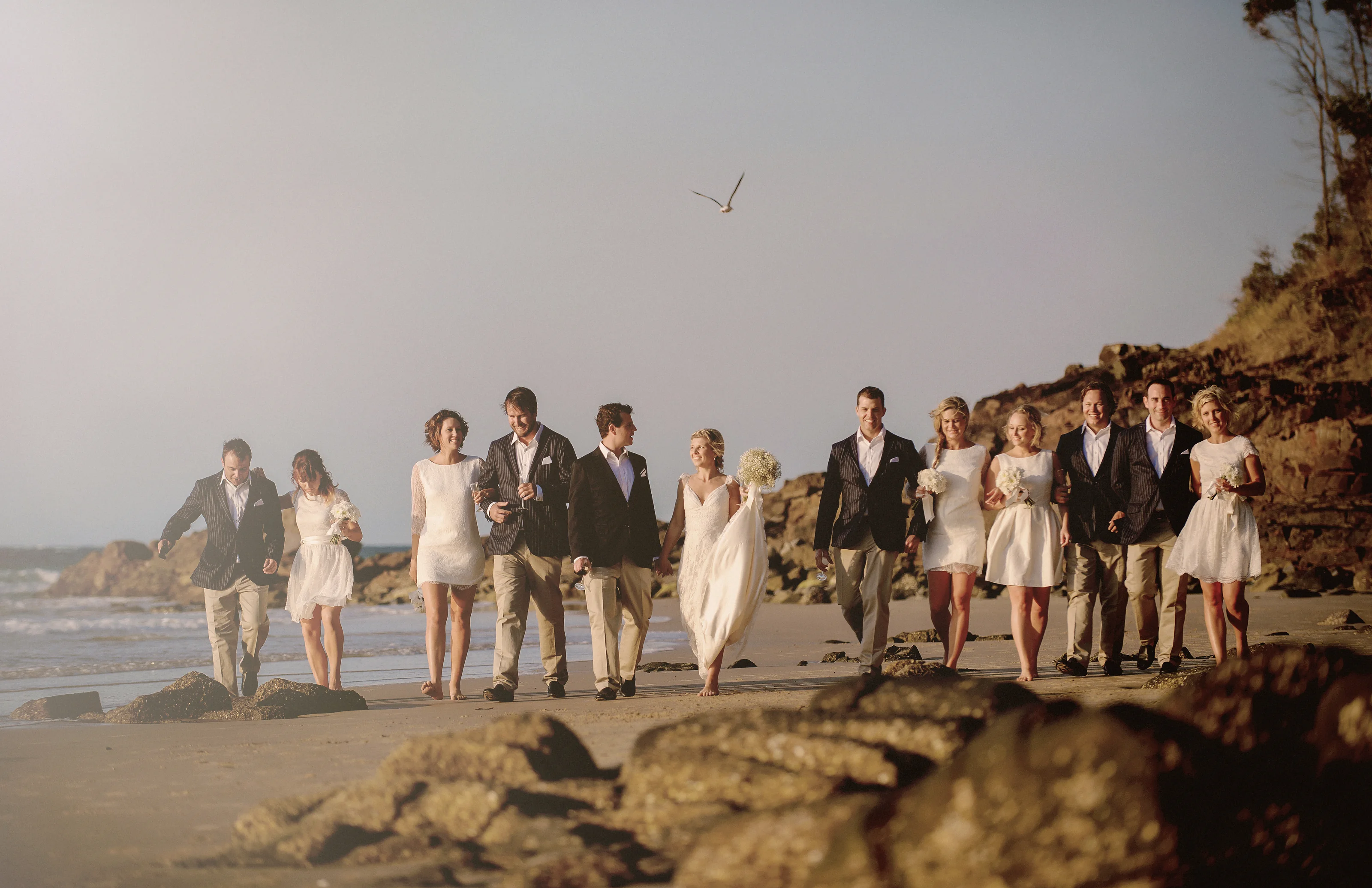 The couple and their bridal party walk together along Little Cove beach in Noosa in warm evening light.