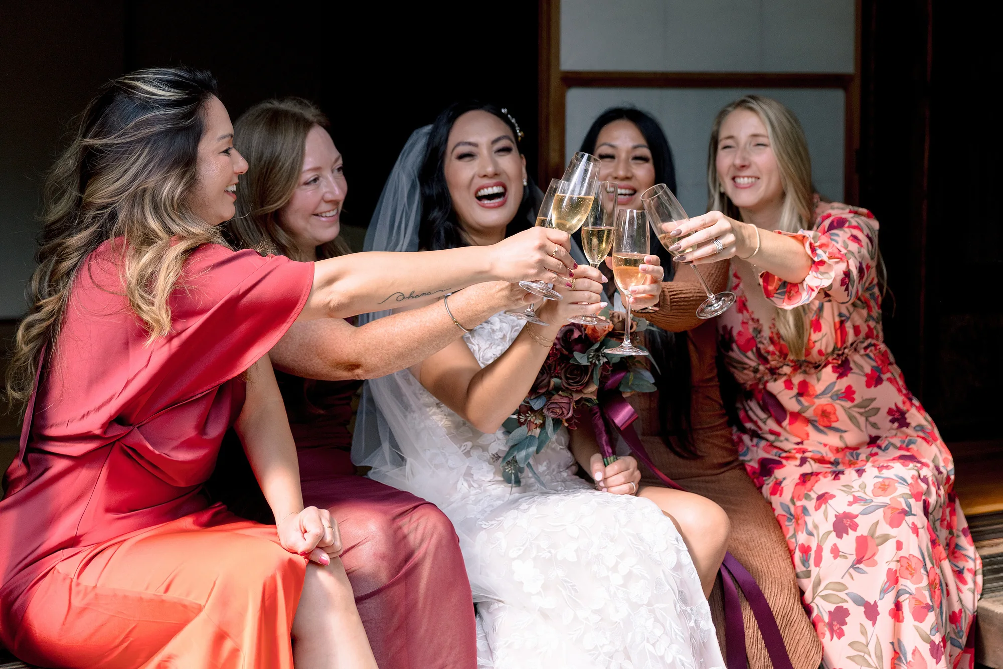 The bride and her friends clink champagne glasses, laughing.