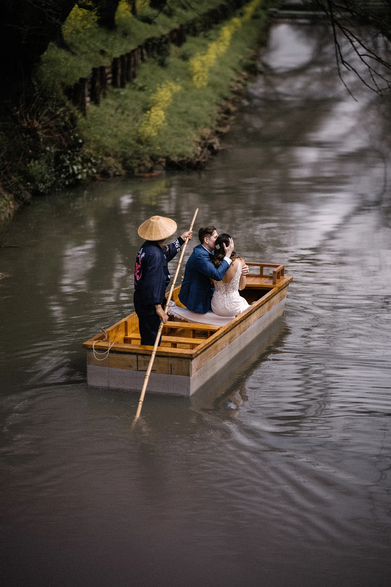 A boatman poles a small boat along a canal, the couple under a paper umbrella.