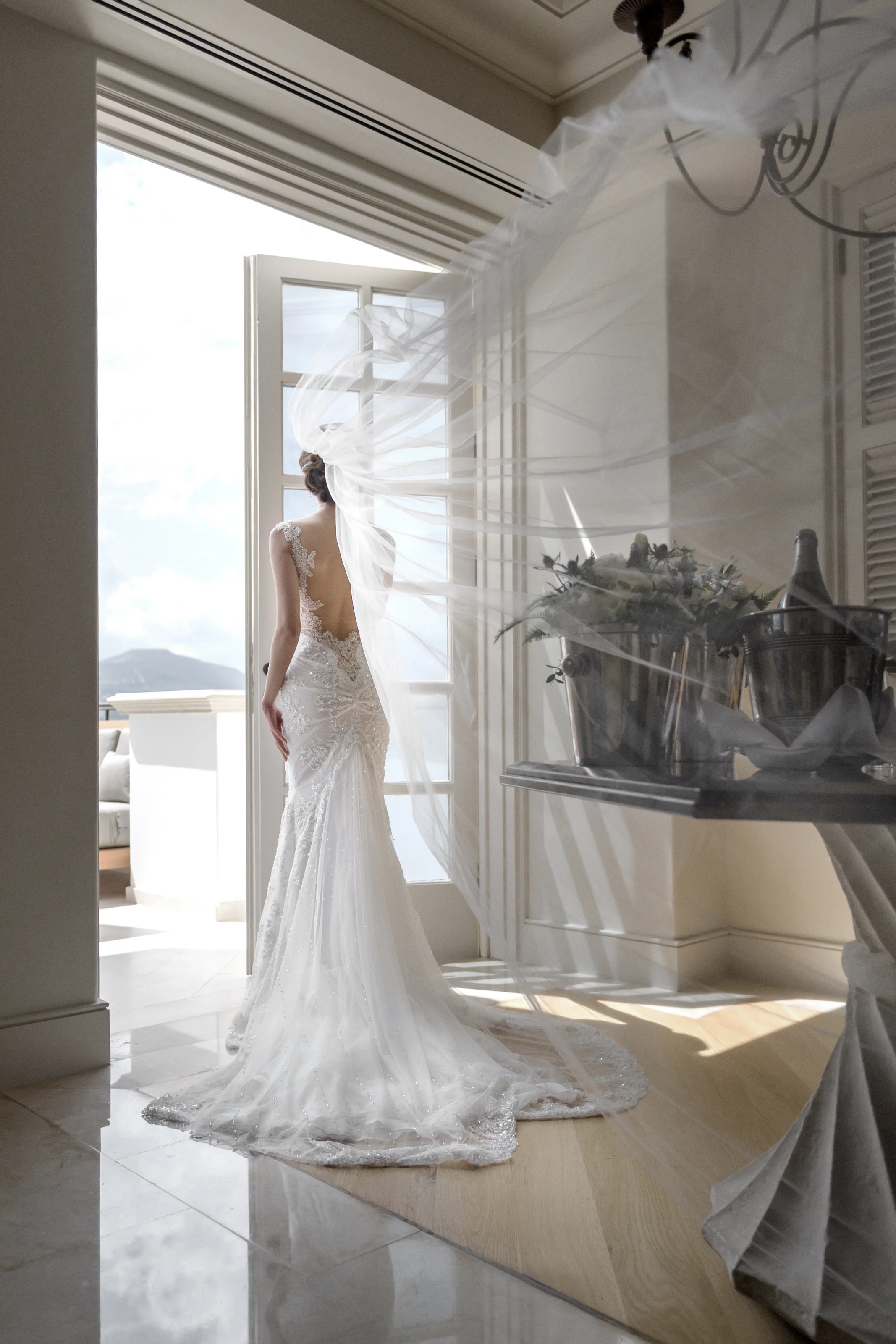 The bride stands at an open balcony door, her veil drifting in the sea breeze, in Cyprus.
