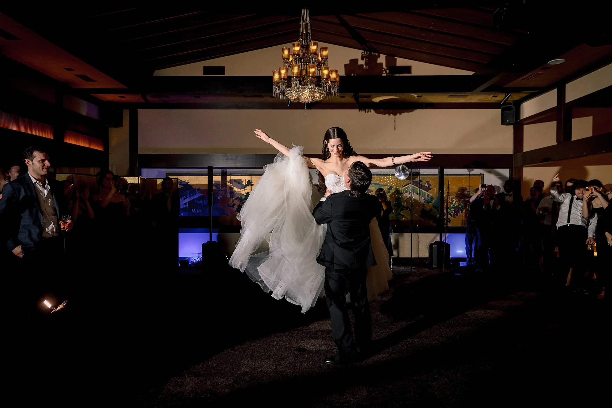 The groom dips the bride on a crowded dance floor as guests cheer around them.