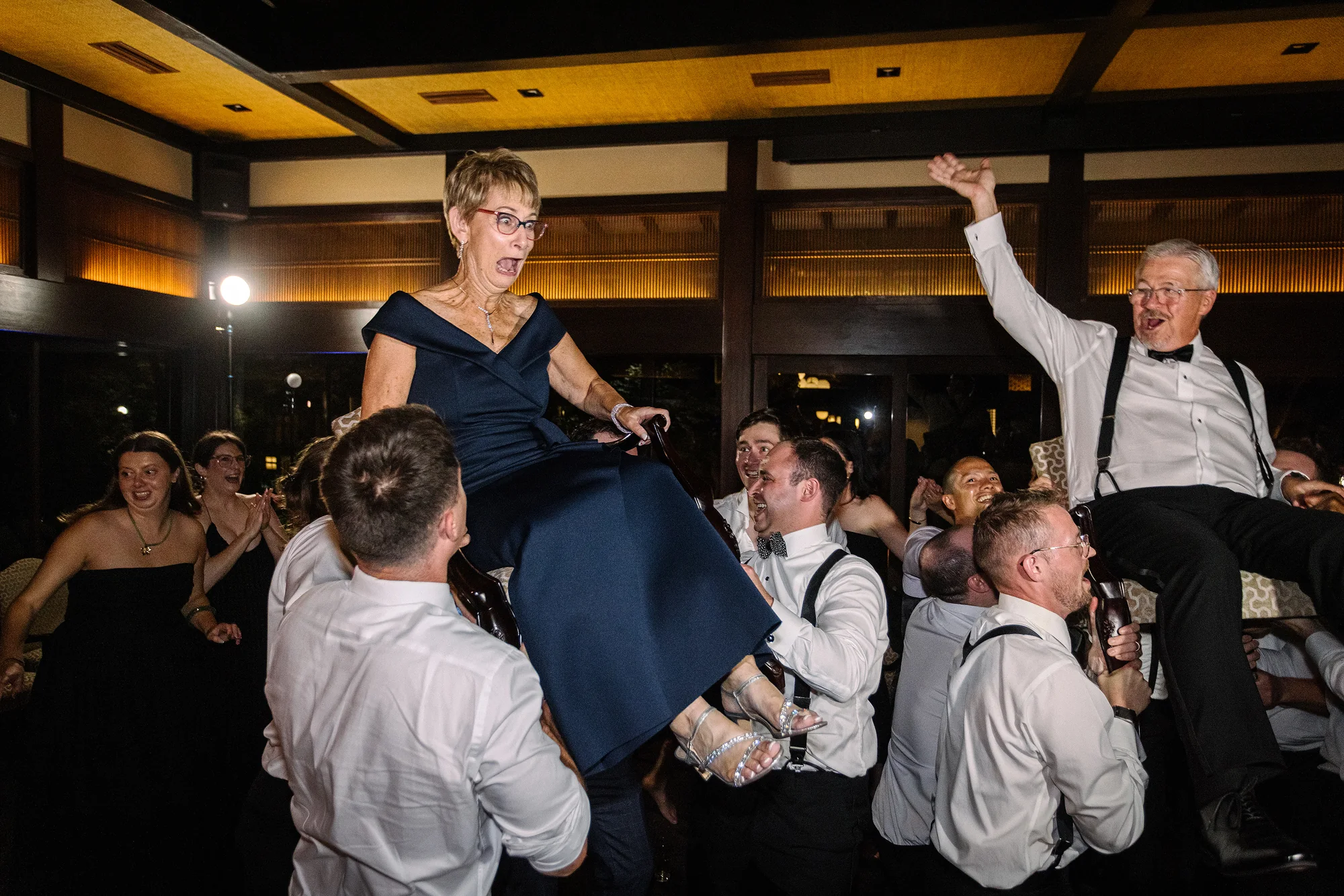 A beaming guest in navy is lifted high on the dance floor as everyone around her cheers.