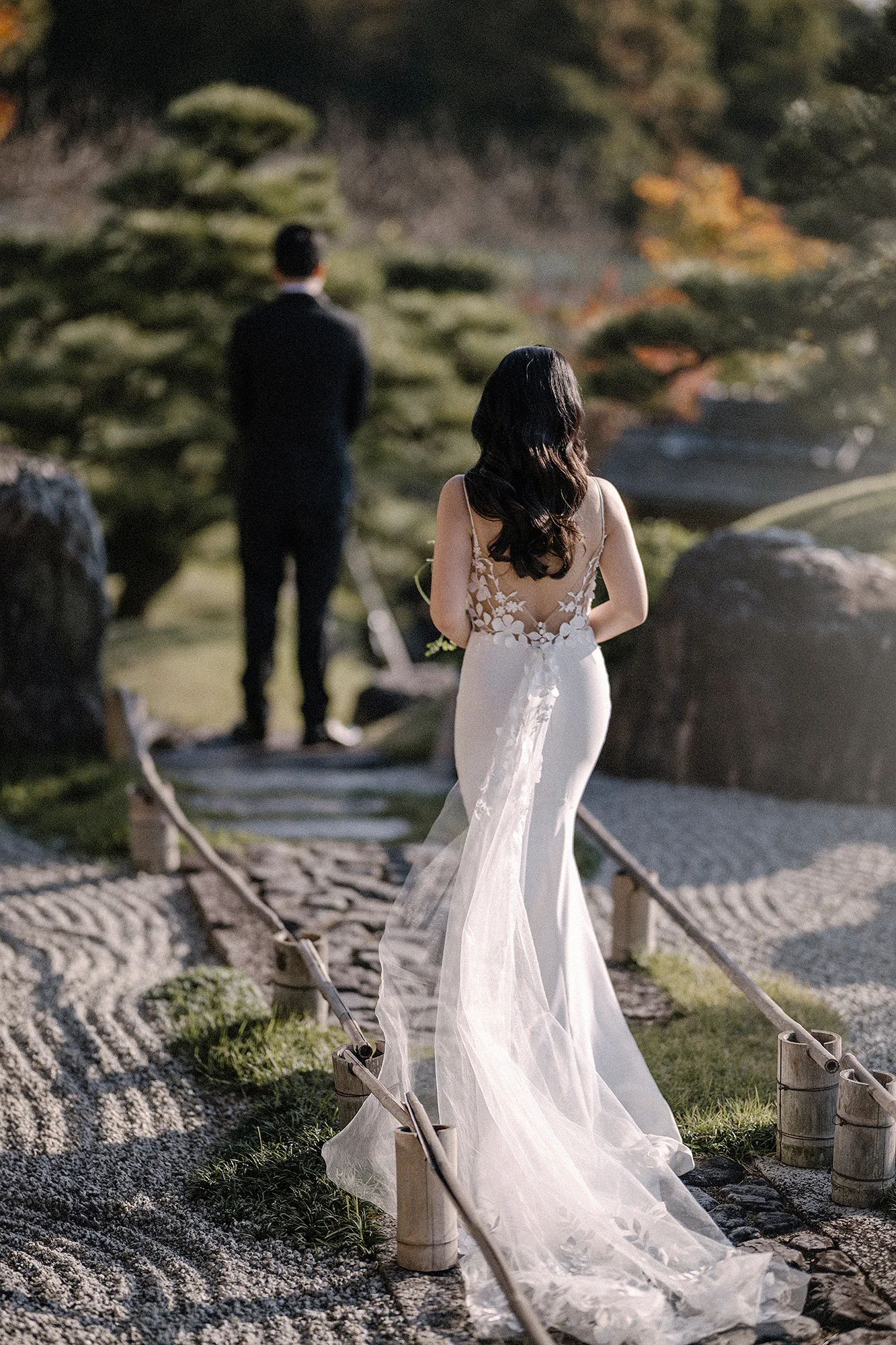 The bride walks up behind the groom on a stone path through a raked dry garden in Kyoto for their first look.