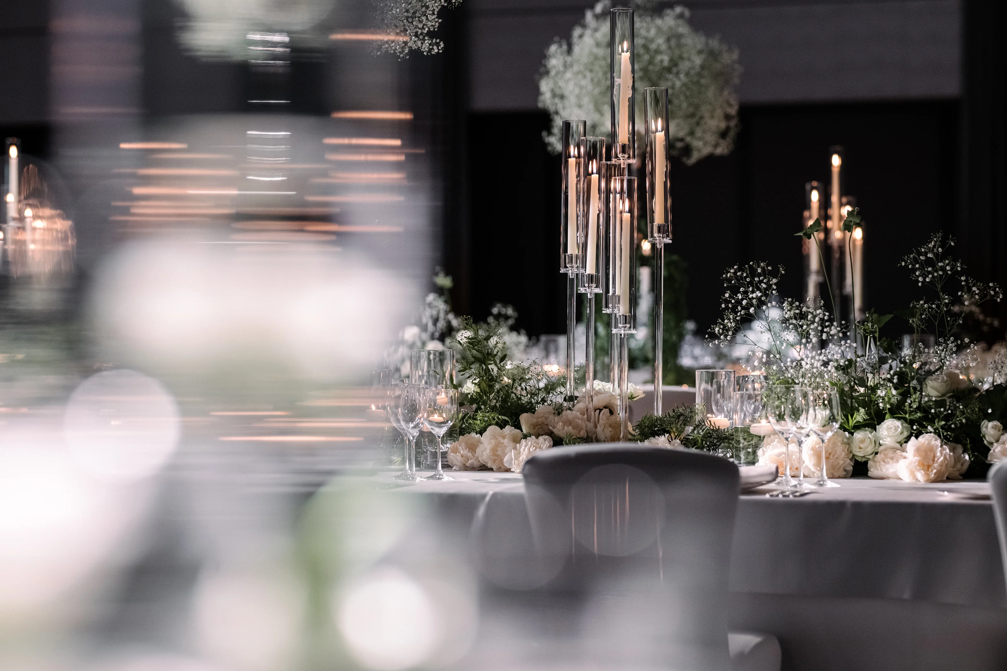 Tall glass candelabras and white roses on a reception table at Four Seasons Otemachi, the room softly lit beyond.