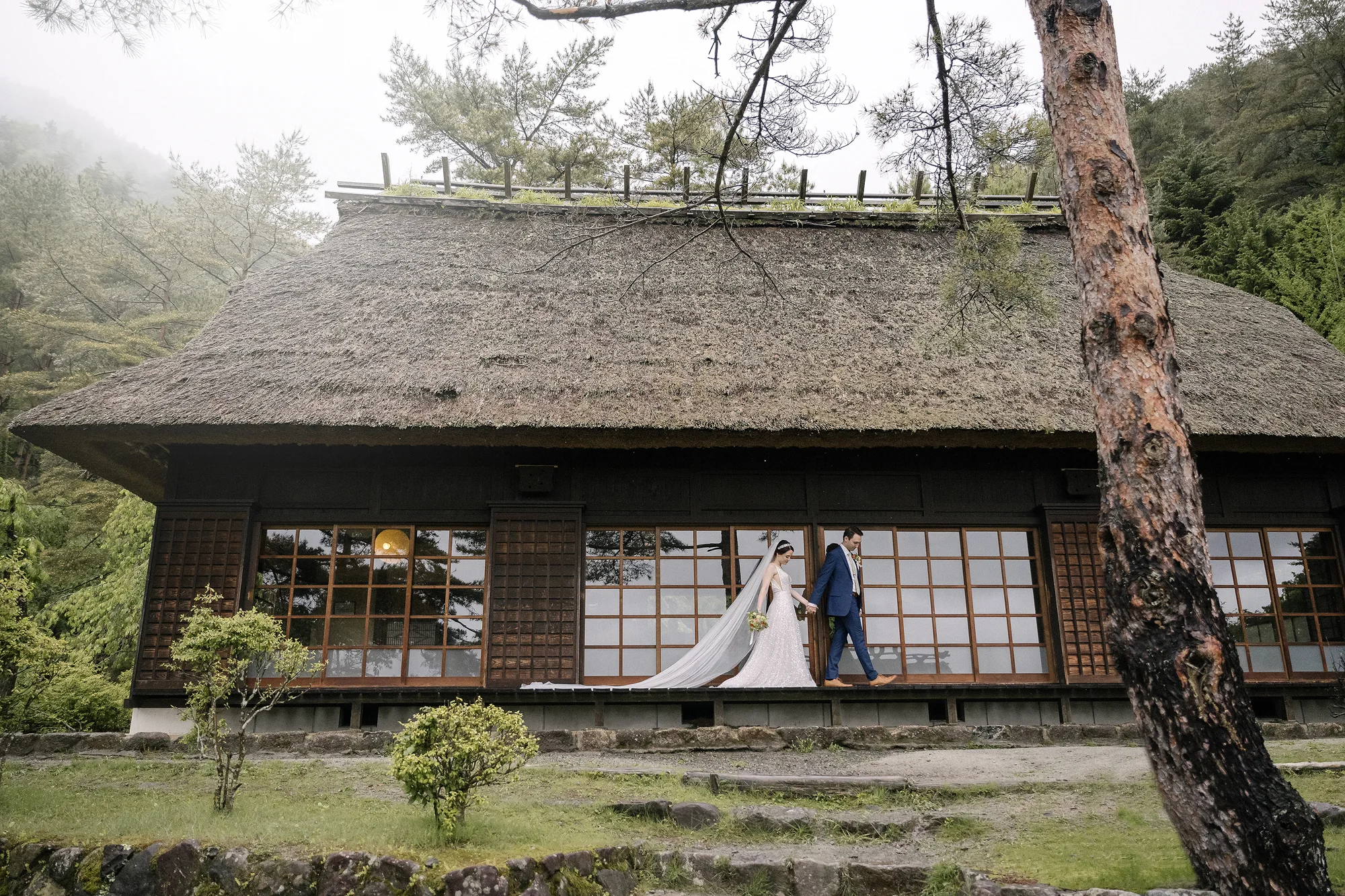 The couple stand before a thatched farmhouse in a village in the Fuji Five Lakes.