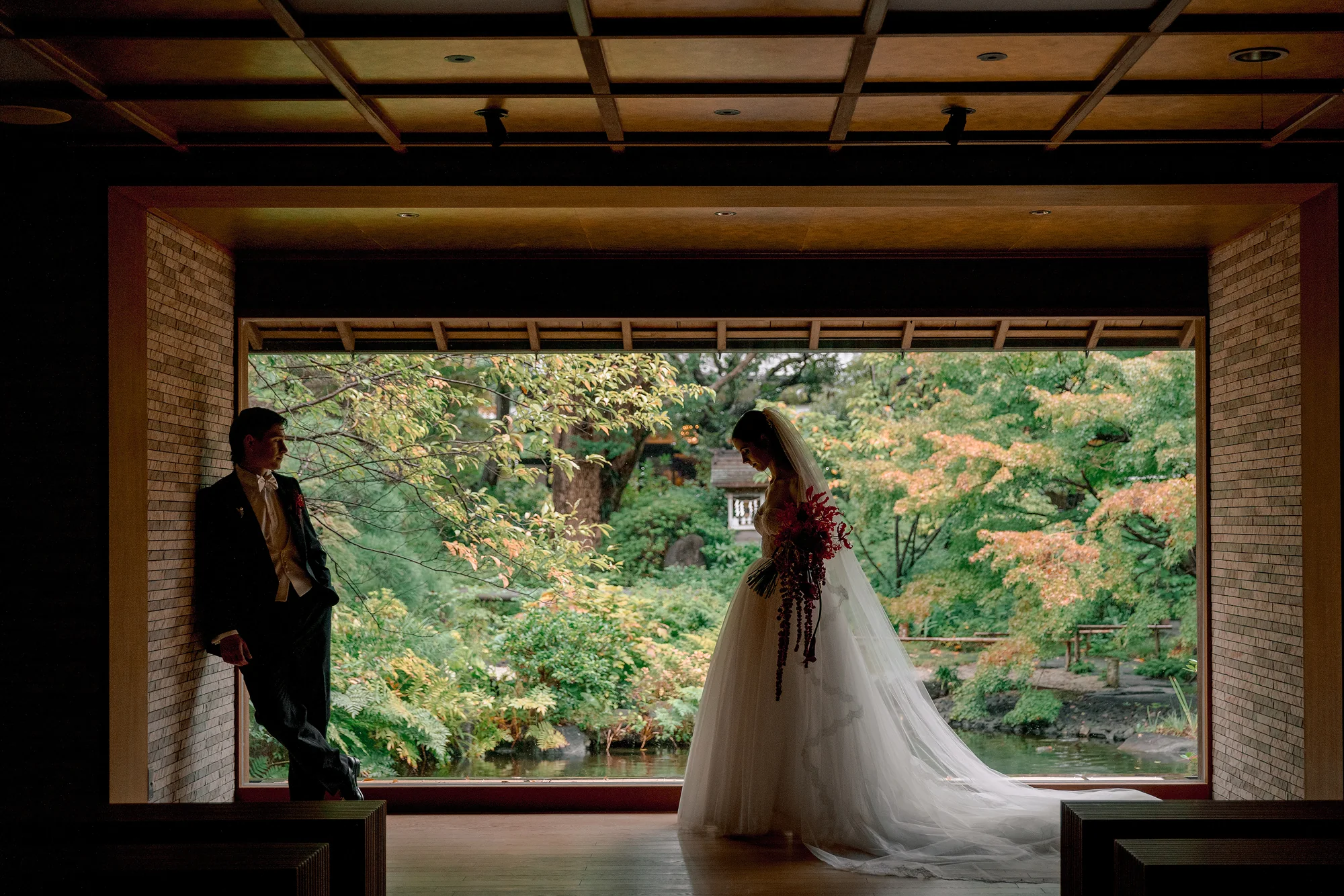A couple stand in a wide opening onto a green garden, framed in dark timber.
