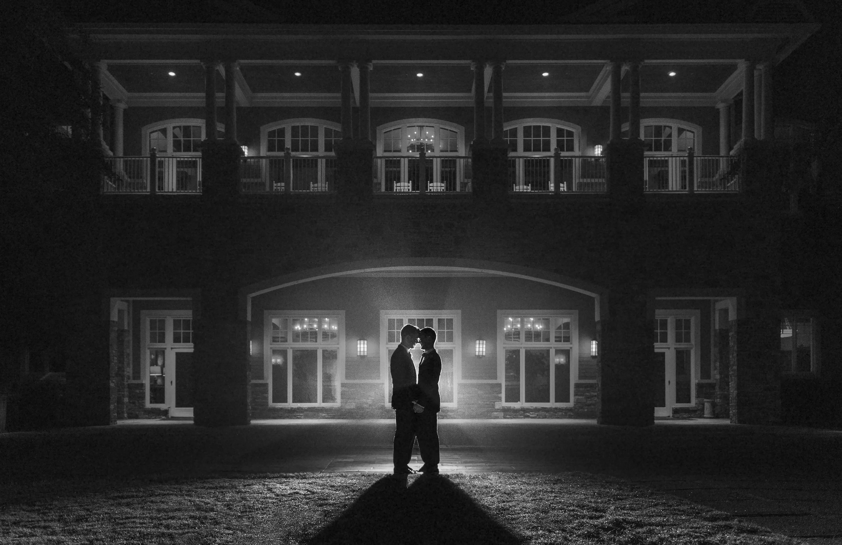 In black and white, the couple stand together in a pool of light outside a grand building at night in Georgia.