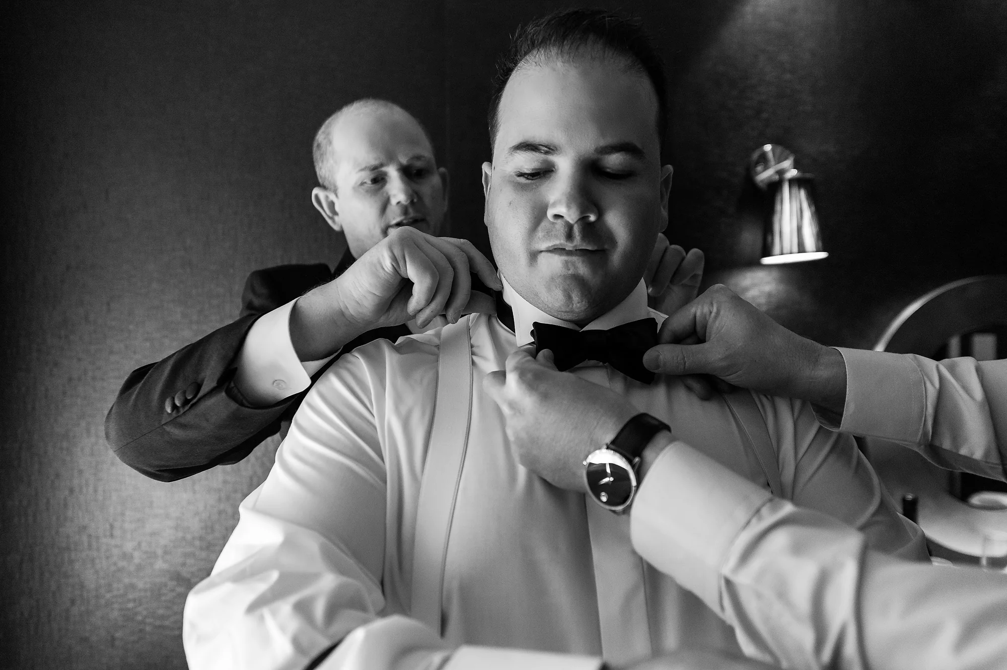In black and white, a friend straightens the groom's bow tie as he gets ready in Karuizawa.
