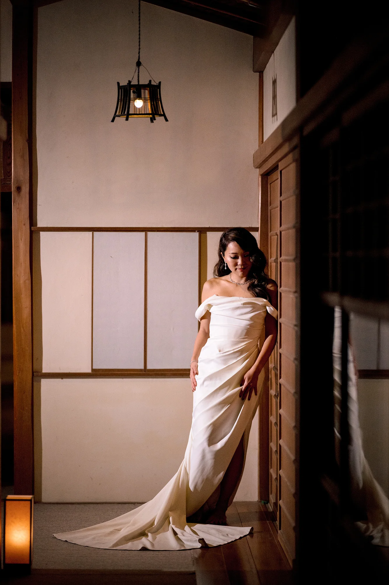 The bride leans in a doorway along a lantern-lit wooden corridor in Hakone.