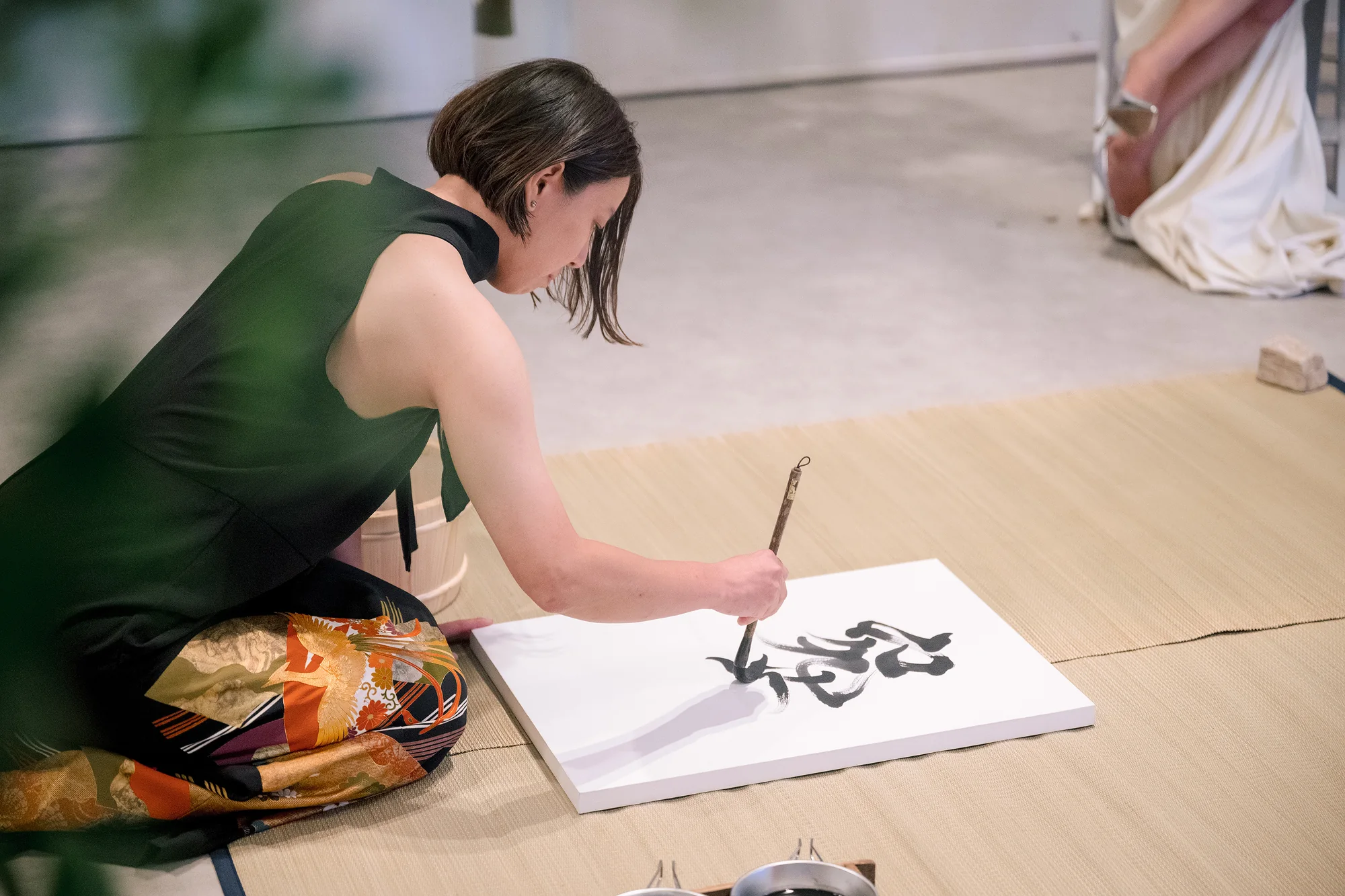A calligrapher kneels to brush characters onto a white panel during a wedding celebration in Hakone.