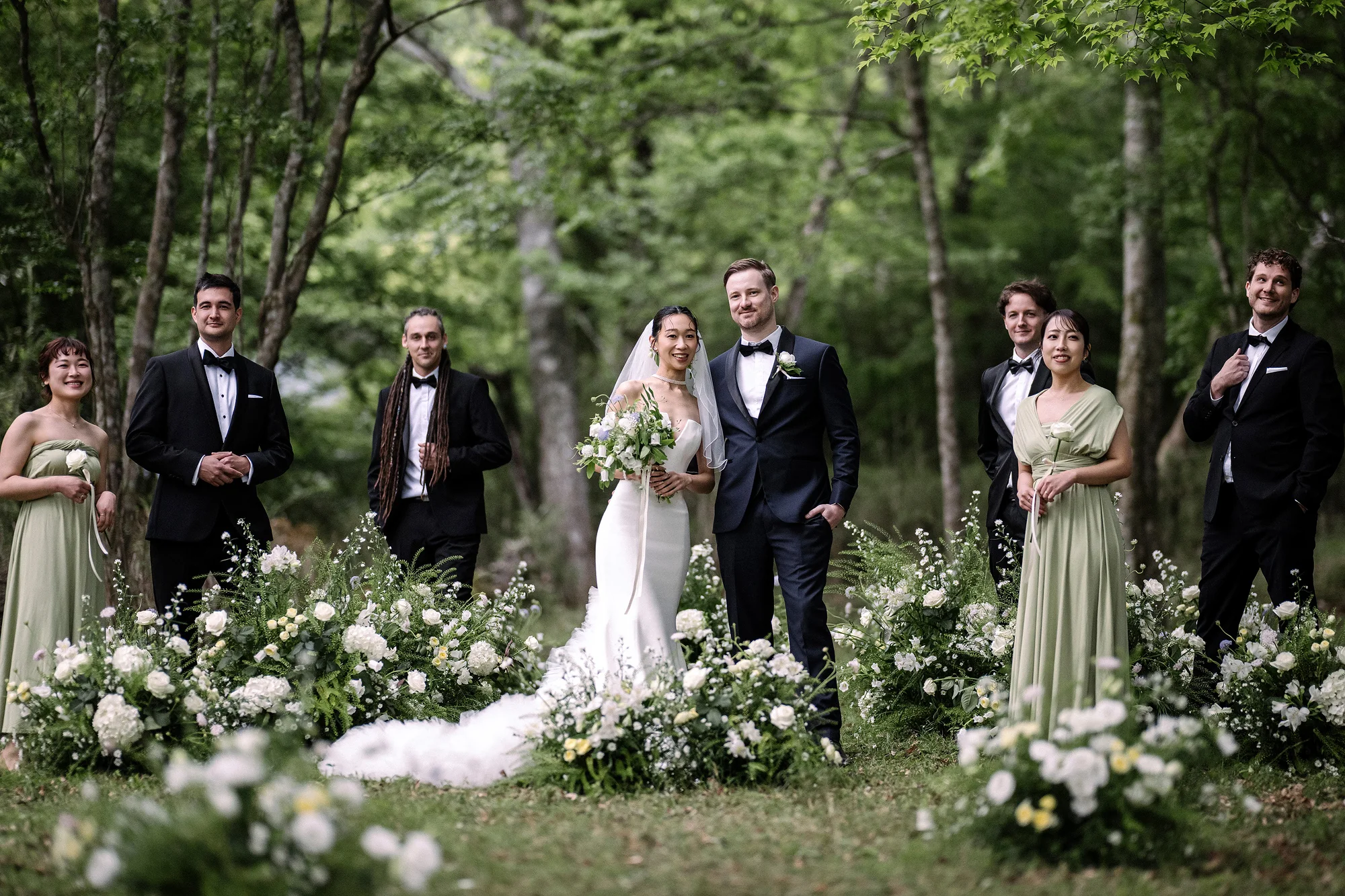 The newlyweds stand with their wedding party among white flowers in a forest clearing in Hakone.