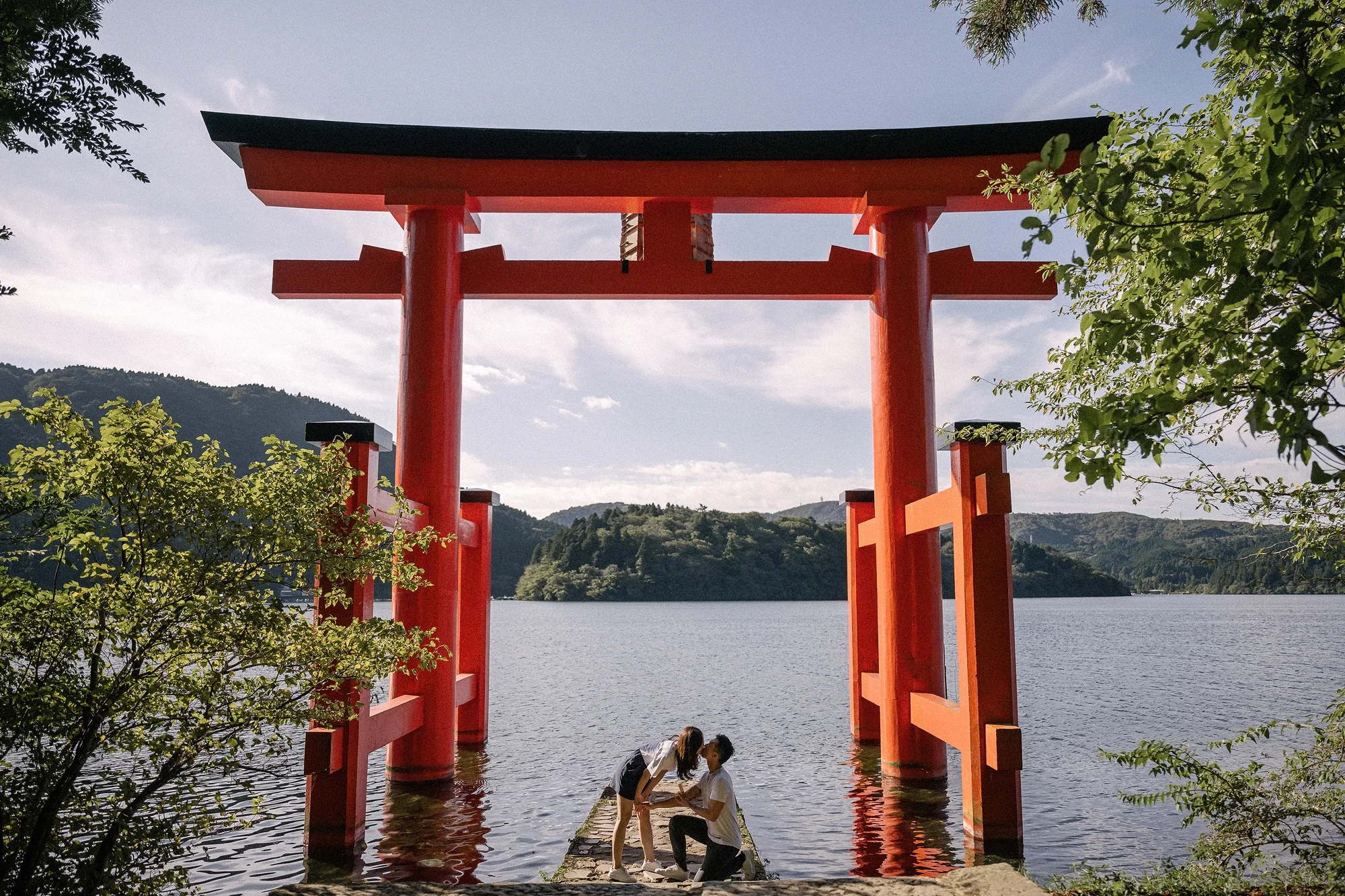 A couple at the foot of the red torii gate standing in Lake Ashi, Hakone.