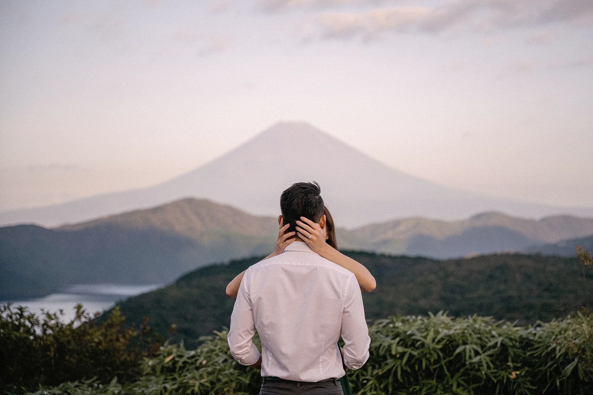 A couple embrace above the hills of Hakone, Mt Fuji in pale evening light.