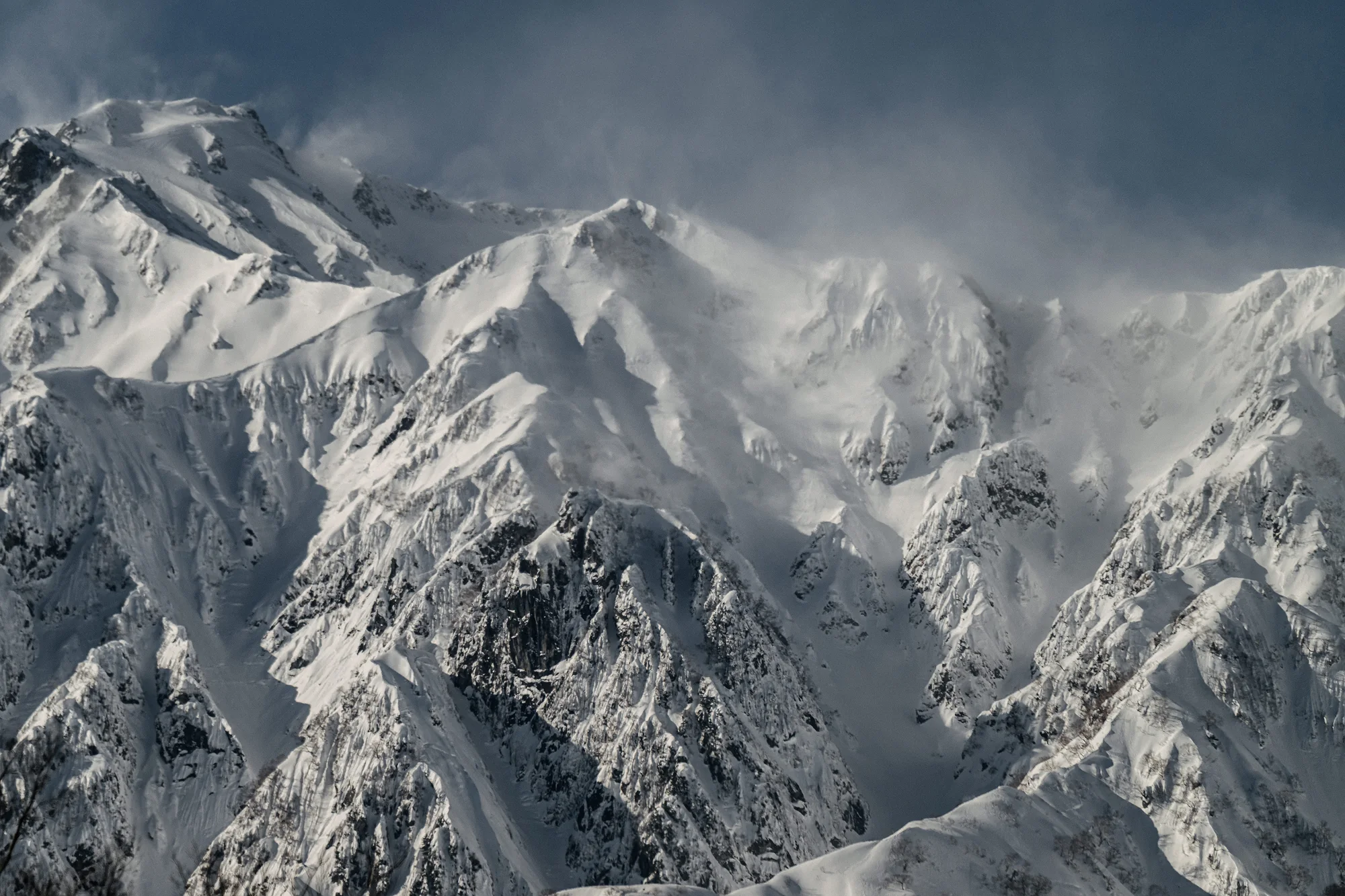 Snow-covered peaks of the Japanese Alps, wind lifting snow from the ridges.