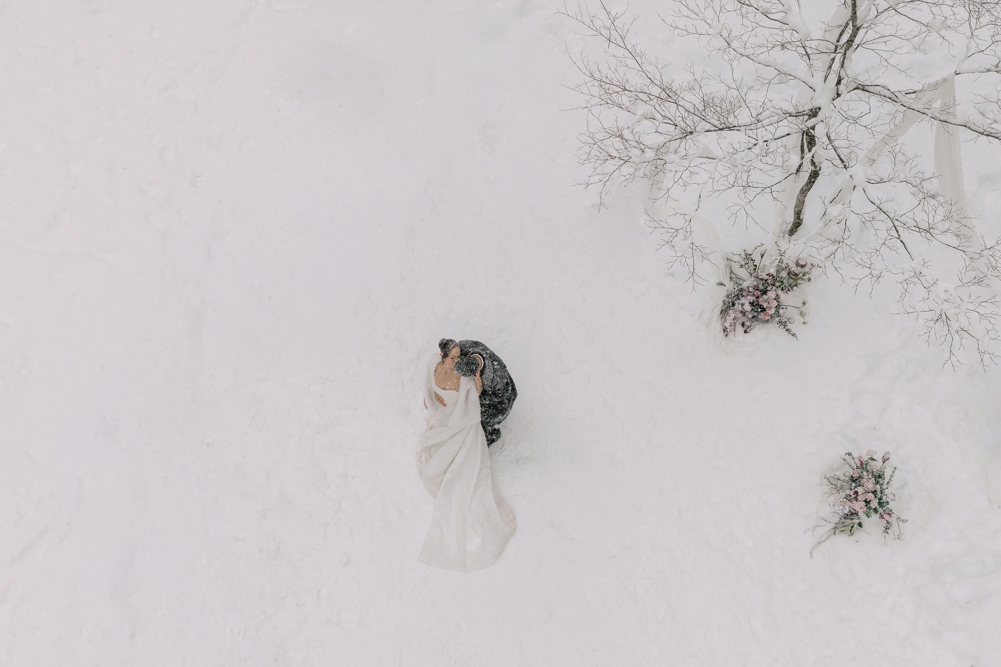 Newlyweds embracing in heavy snowfall among trees in Hakuba.