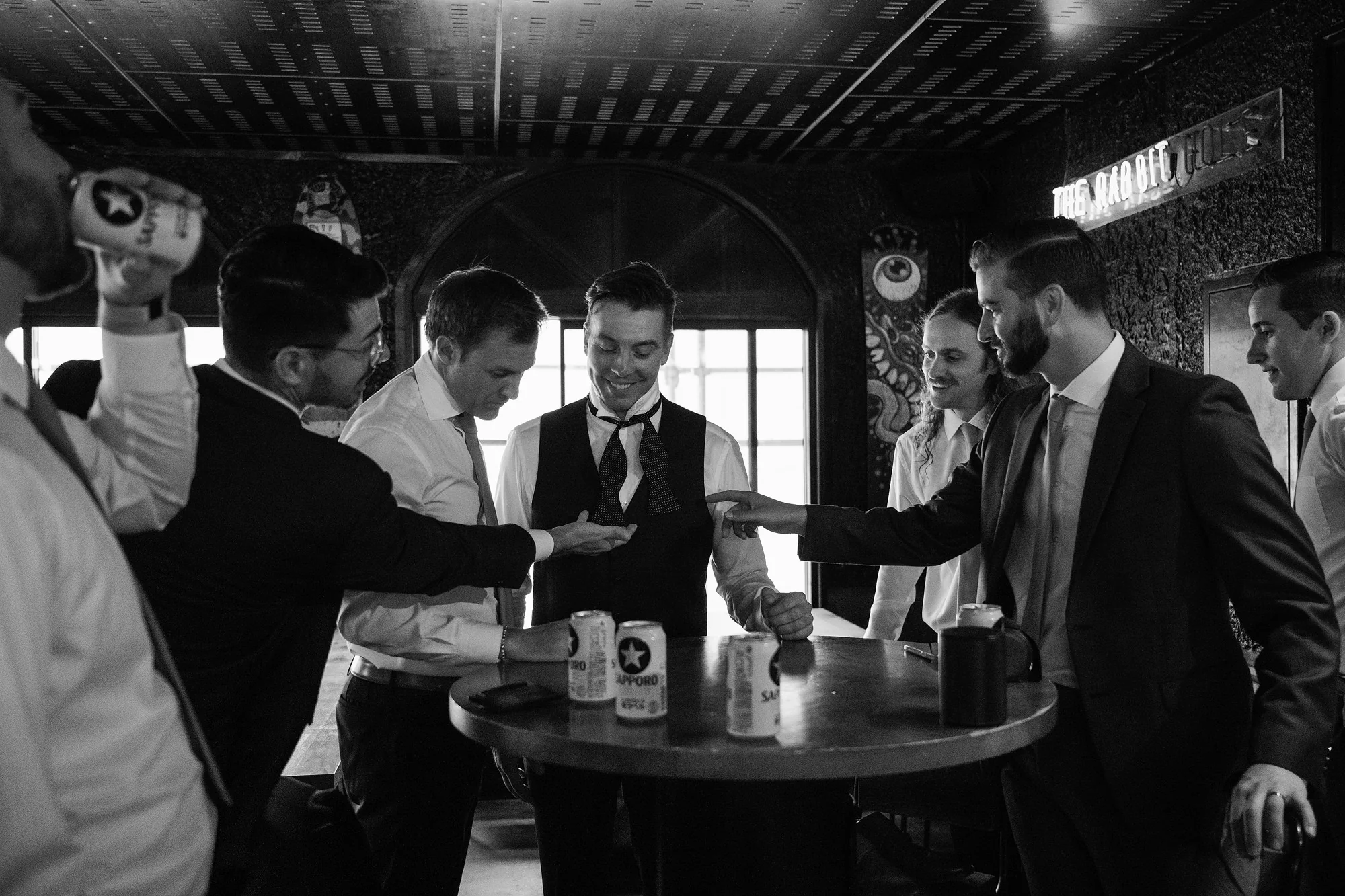 In black and white, the groom and his groomsmen gather around a table, laughing, before the ceremony in Hakuba.