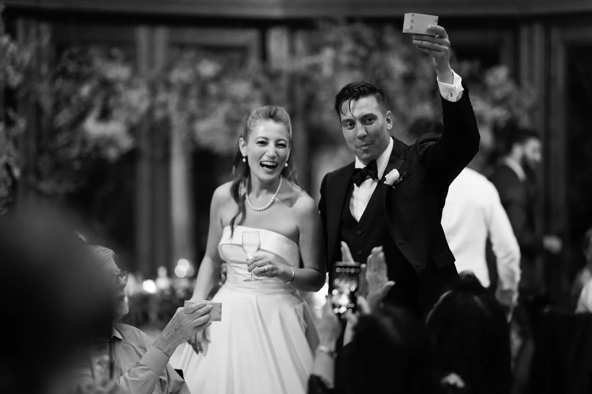 In black and white, the groom raises his glass as the bride laughs with their guests in Hakuba.