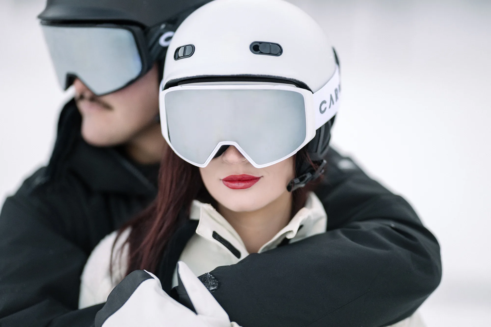 A couple in ski goggles lean close in the snow.