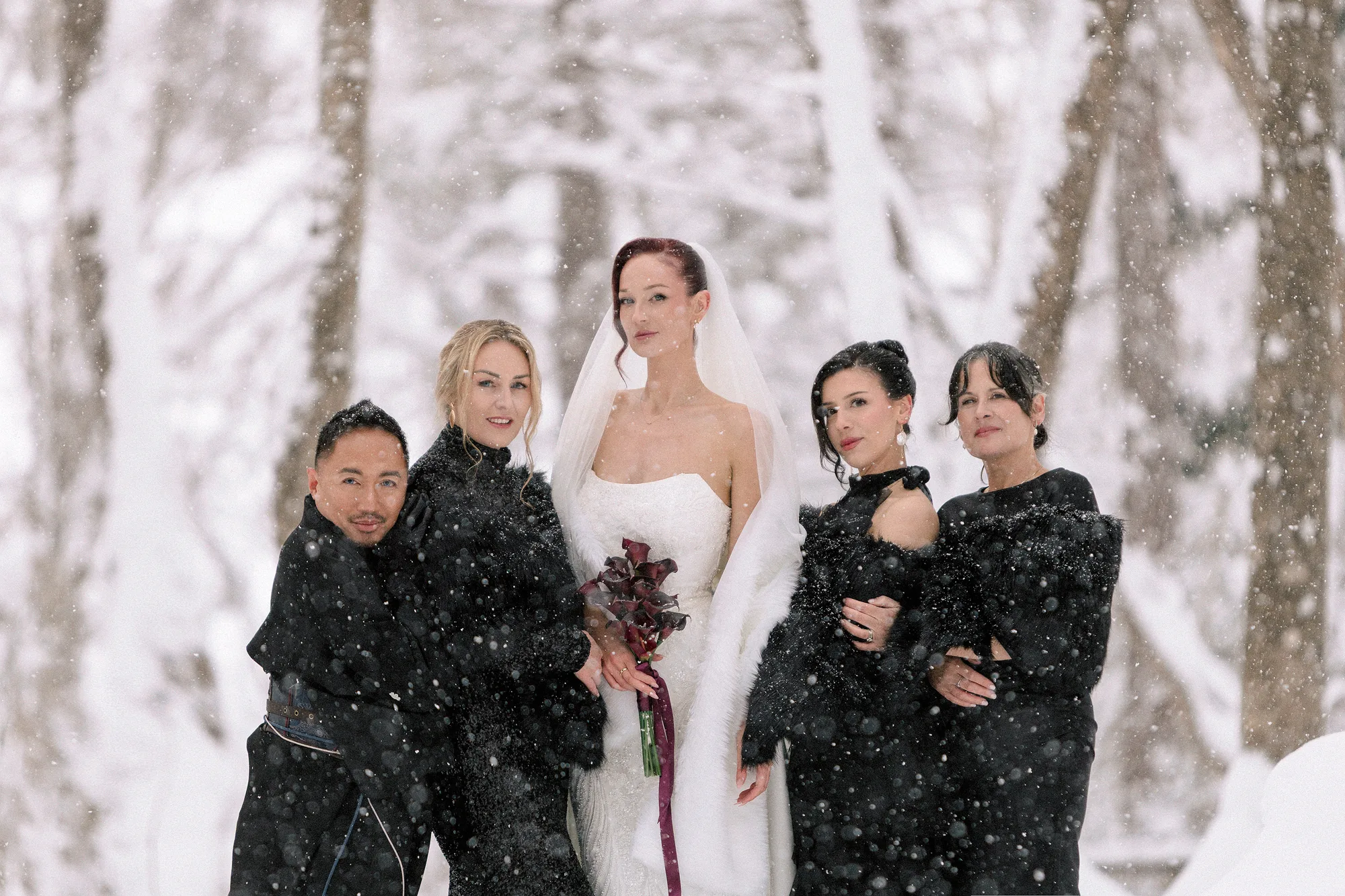 A bride celebrates with friends in falling snow.