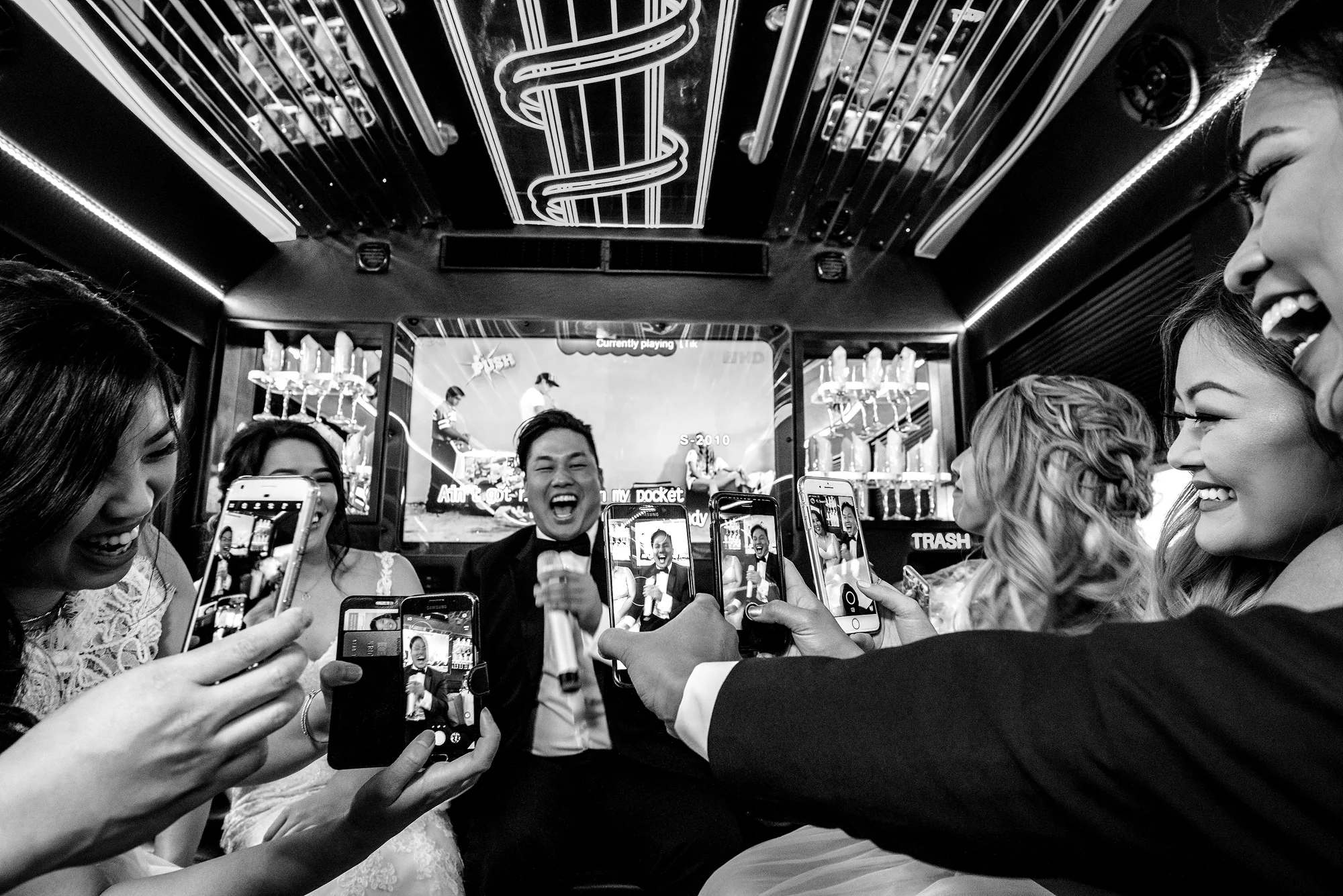 In black and white, guests crowd around the couple with their phones up, laughing, at a reception in Houston.