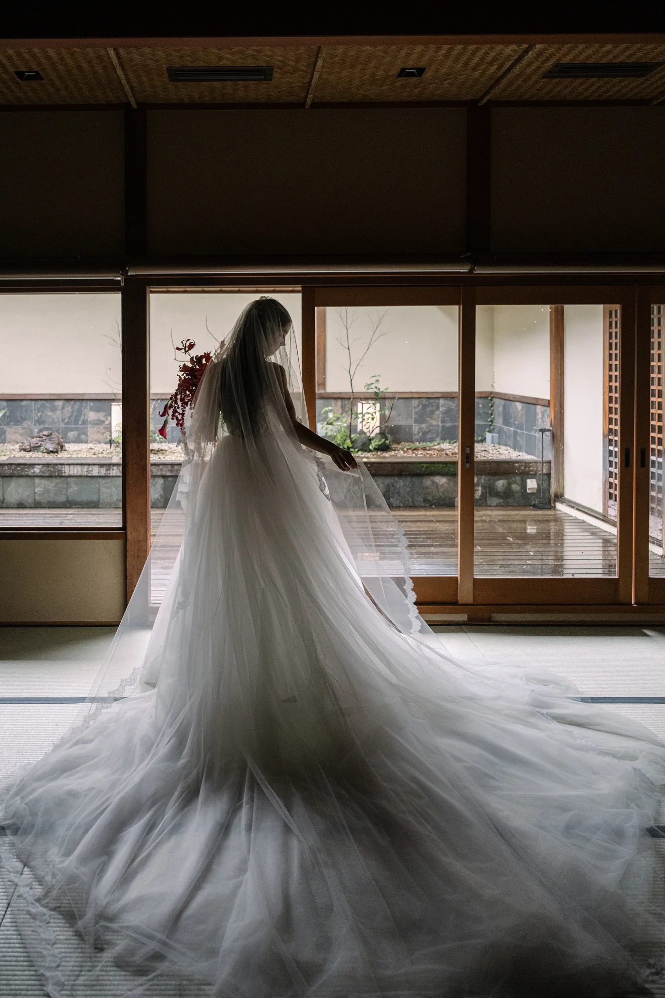 The bride stands with her back to the camera, her train fanned out, looking out to the Japanese garden.