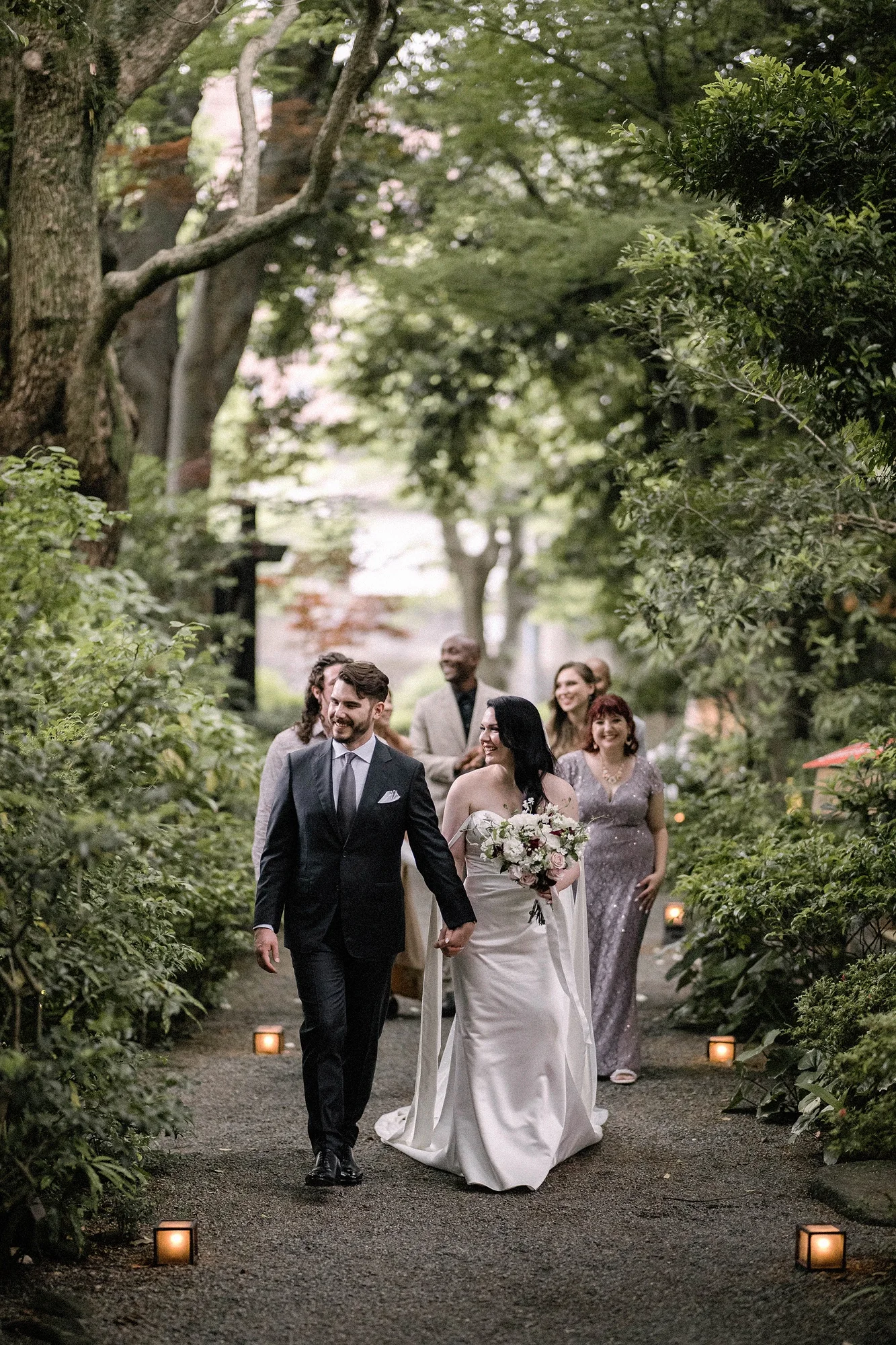 The couple walk a garden path as guests follow.