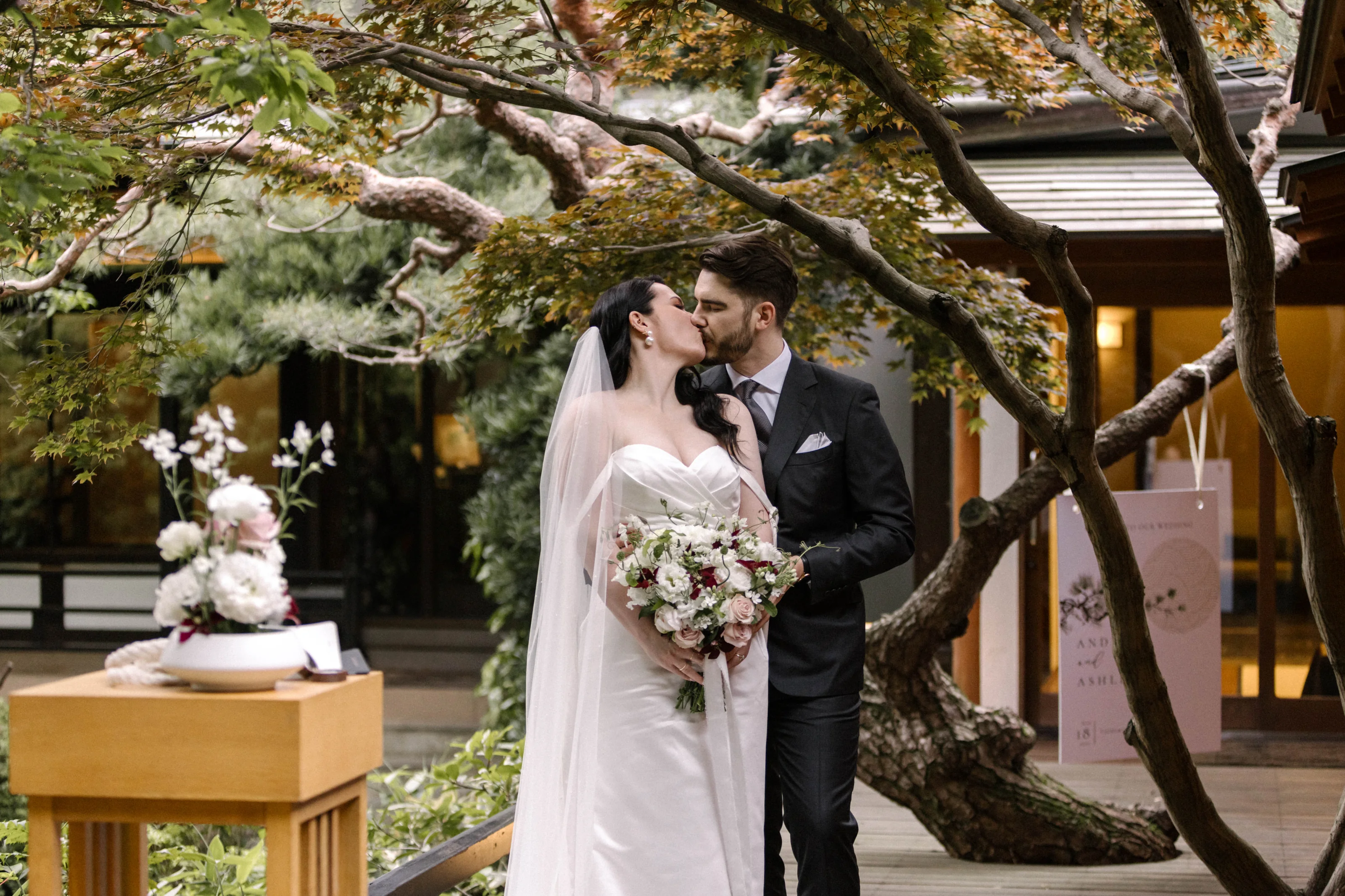 The bride and groom kiss beside the ikebana altar under the maples, a May wedding in Japan in the garden at Jinya.