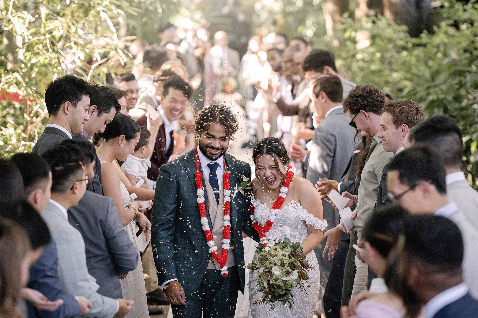 The couple, wearing flower garlands, walk back up the tree-lined aisle as guests shower them with petals.