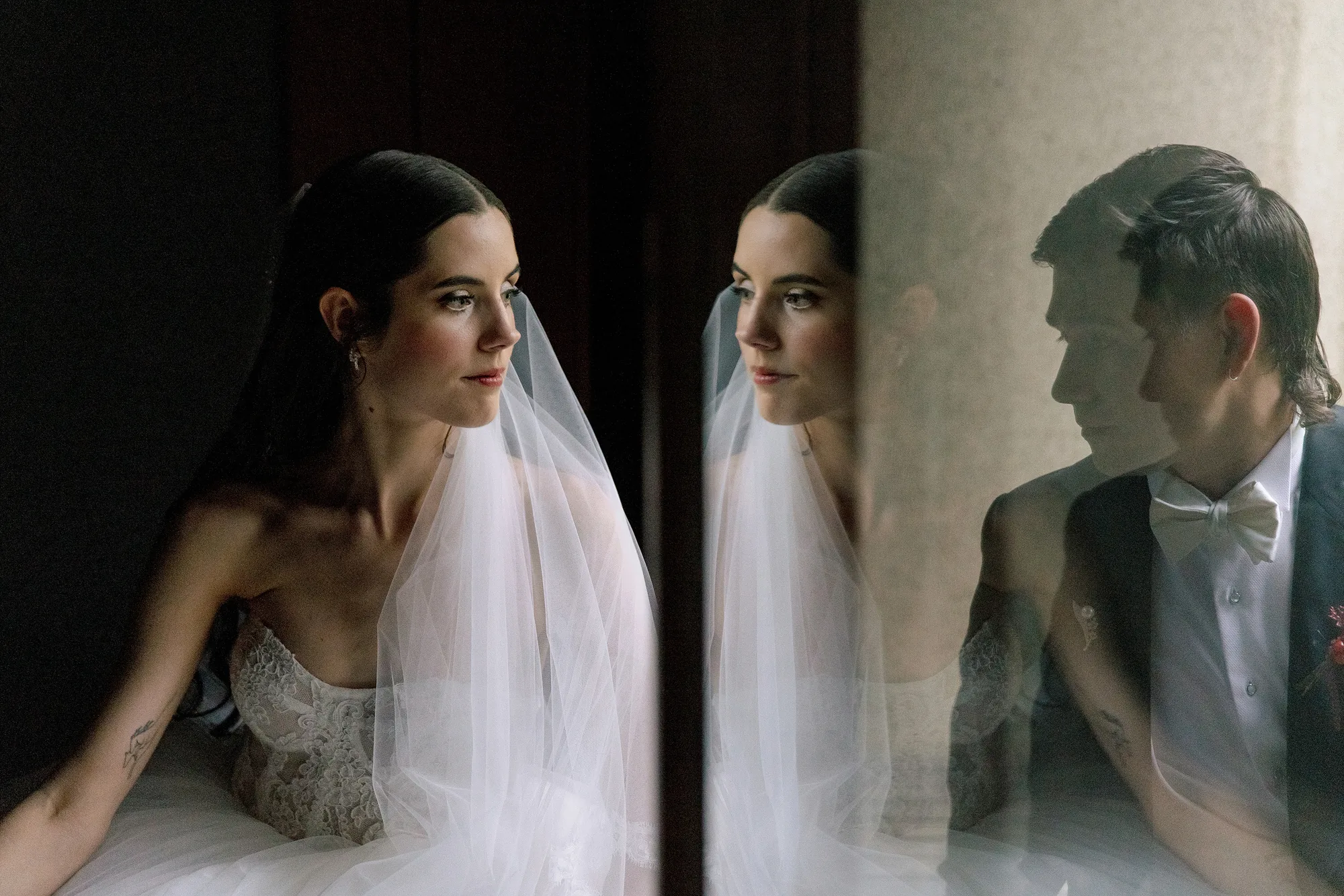 The bride by a window at Jinya, the groom reflected in the glass beside her, a portrait on their wedding day.