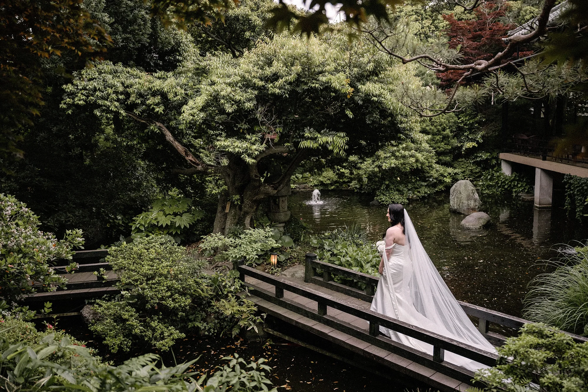 The bride crosses a wooden bridge over the koi pond in the green garden at Jinya, a ryokan wedding at Tsurumaki Onsen in May.