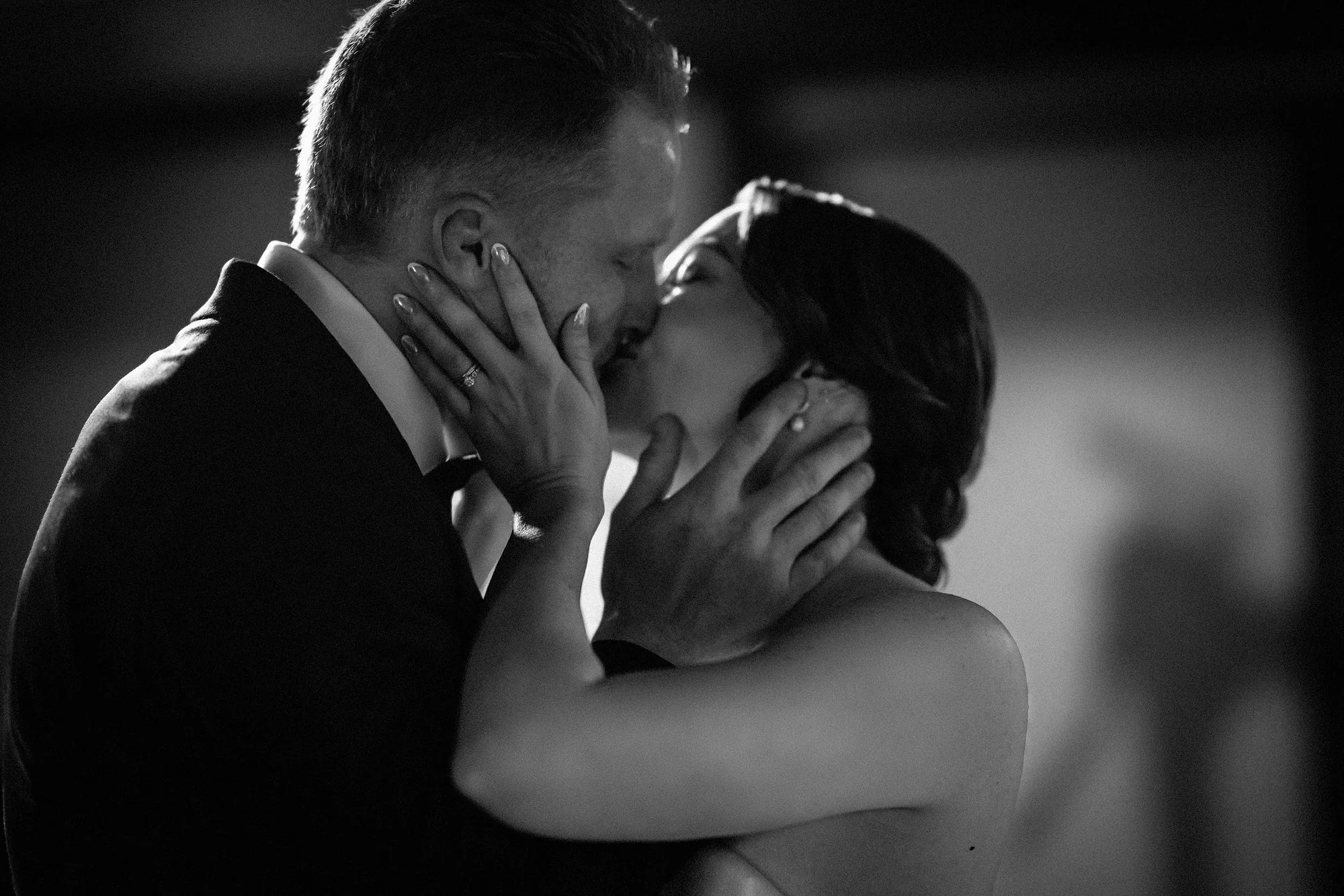 A black and white first dance kiss, the bride's hands holding the groom's face, lit from behind at their intimate wedding at Jinya in Japan.