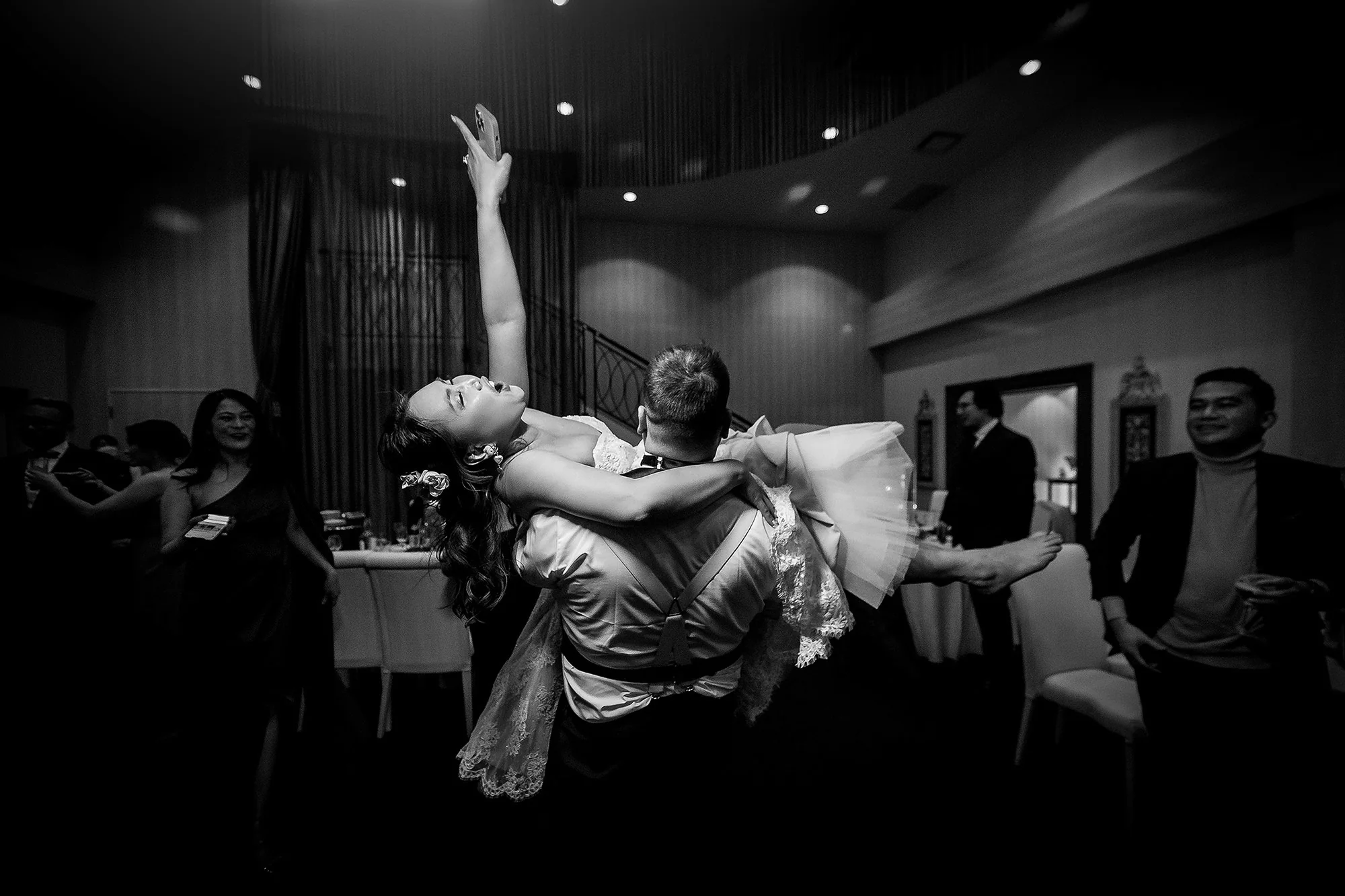 In black and white, the groom swings the bride up on the dance floor, her arm flung high and guests laughing around them, in Karuizawa.