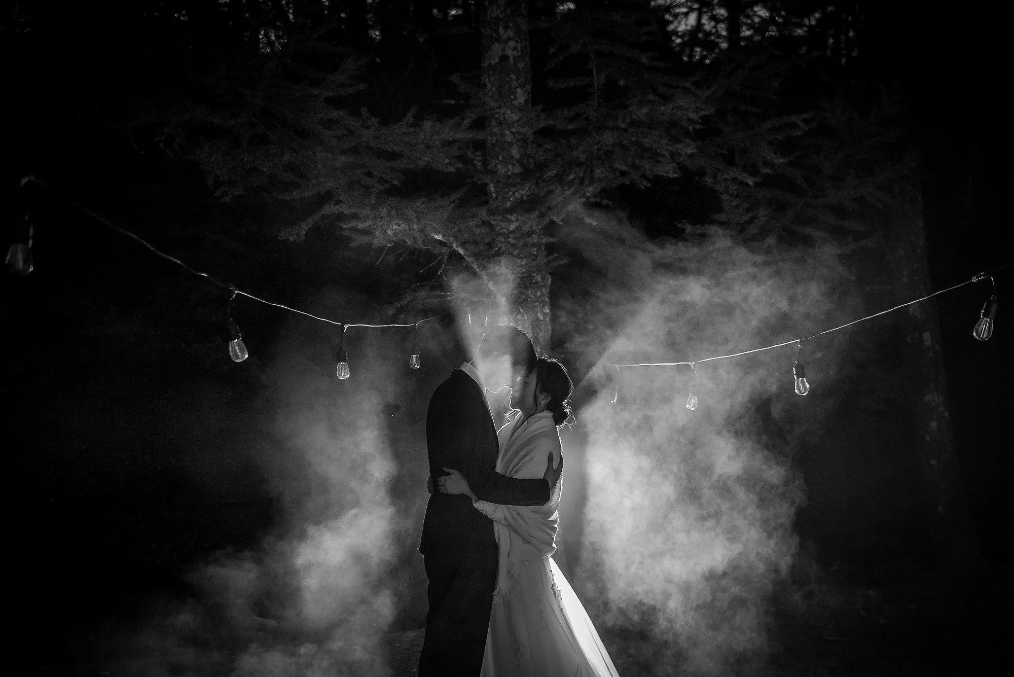 In black and white, the couple hold each other in drifting mist beneath a string of lights at night in Karuizawa.