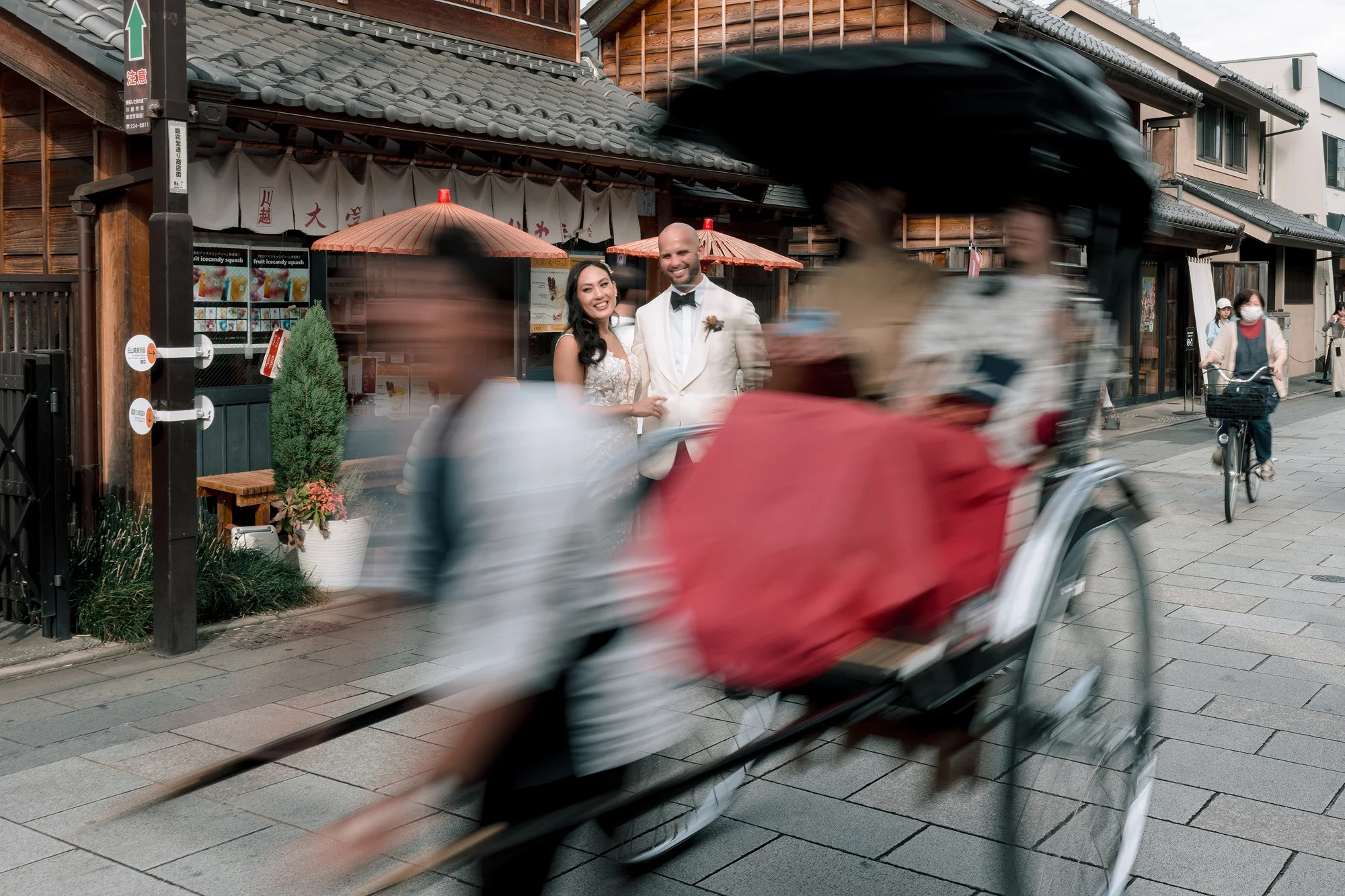 A rickshaw carries the couple down an old merchant street in Kawagoe, the runner a blur of motion.