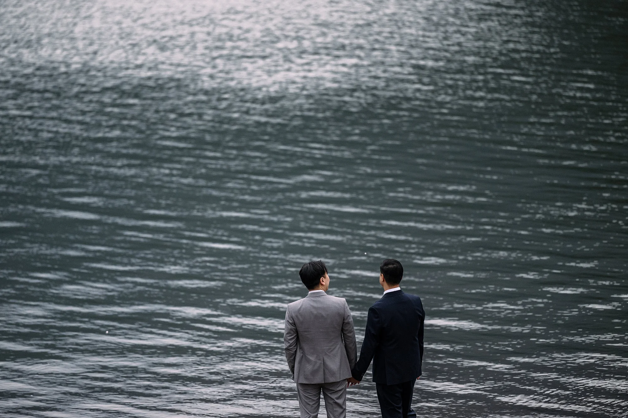 Two grooms stand hand in hand at the edge of Lake Kawaguchi.