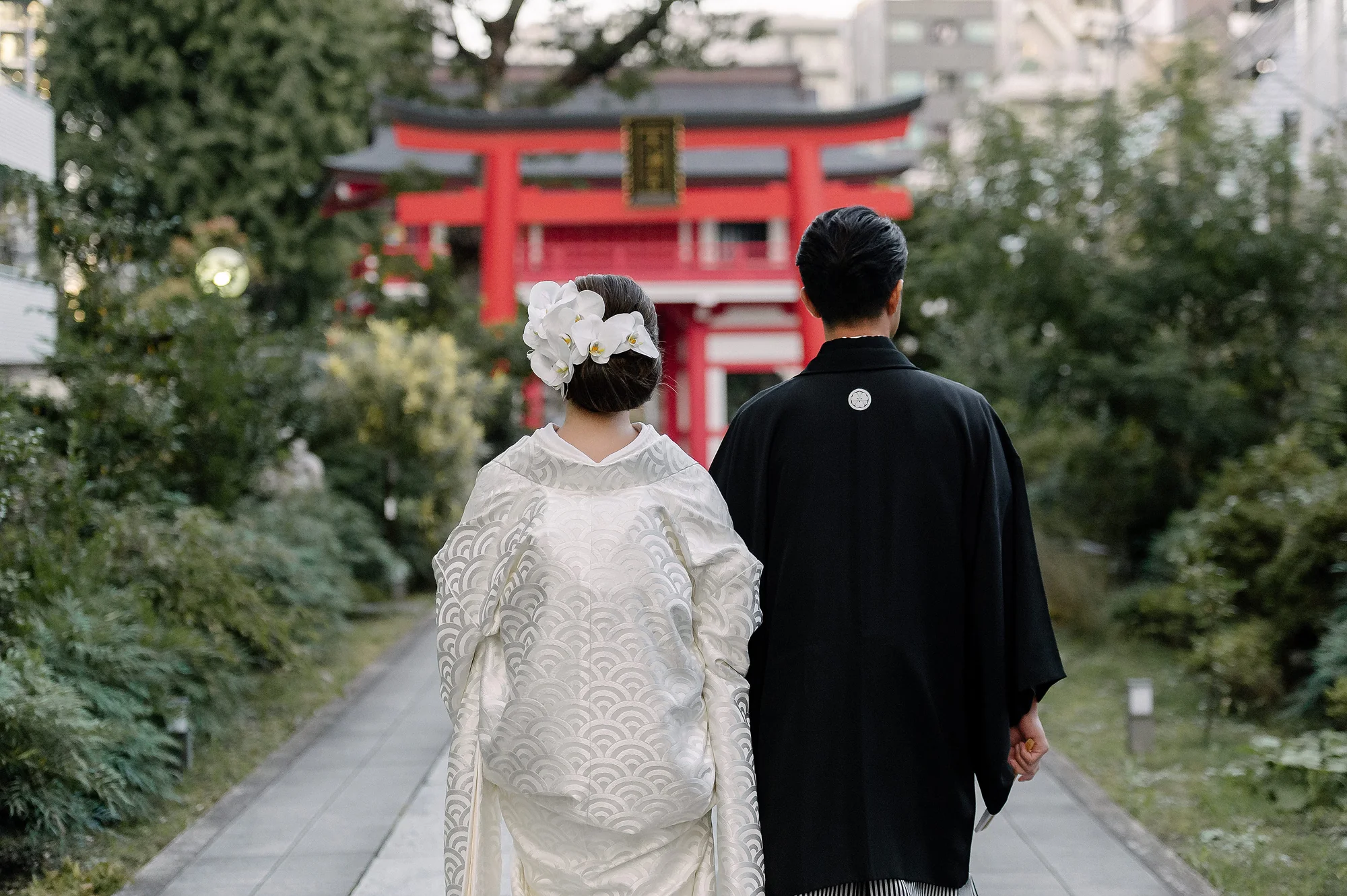 A couple in kimono walk toward a red torii gate.