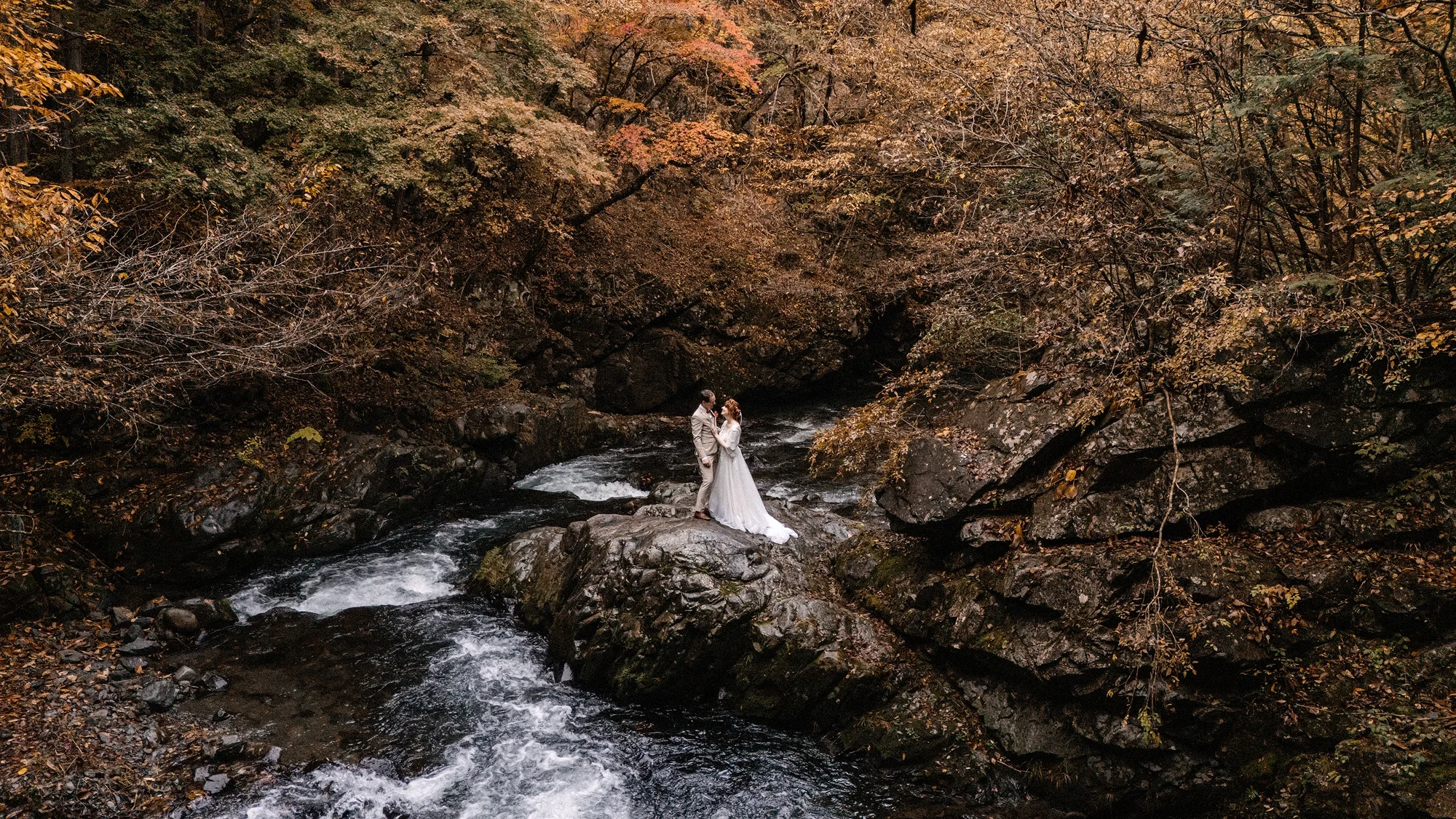 A couple on the rocks of an autumn river gorge.