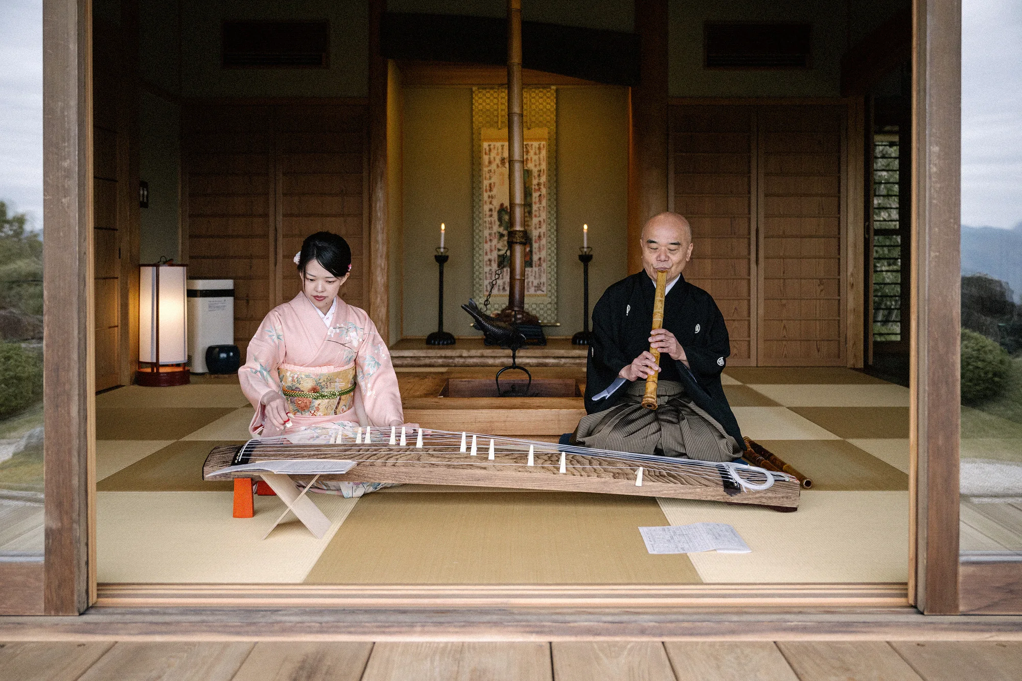 Musicians play koto and shakuhachi in a tatami room open to the garden.