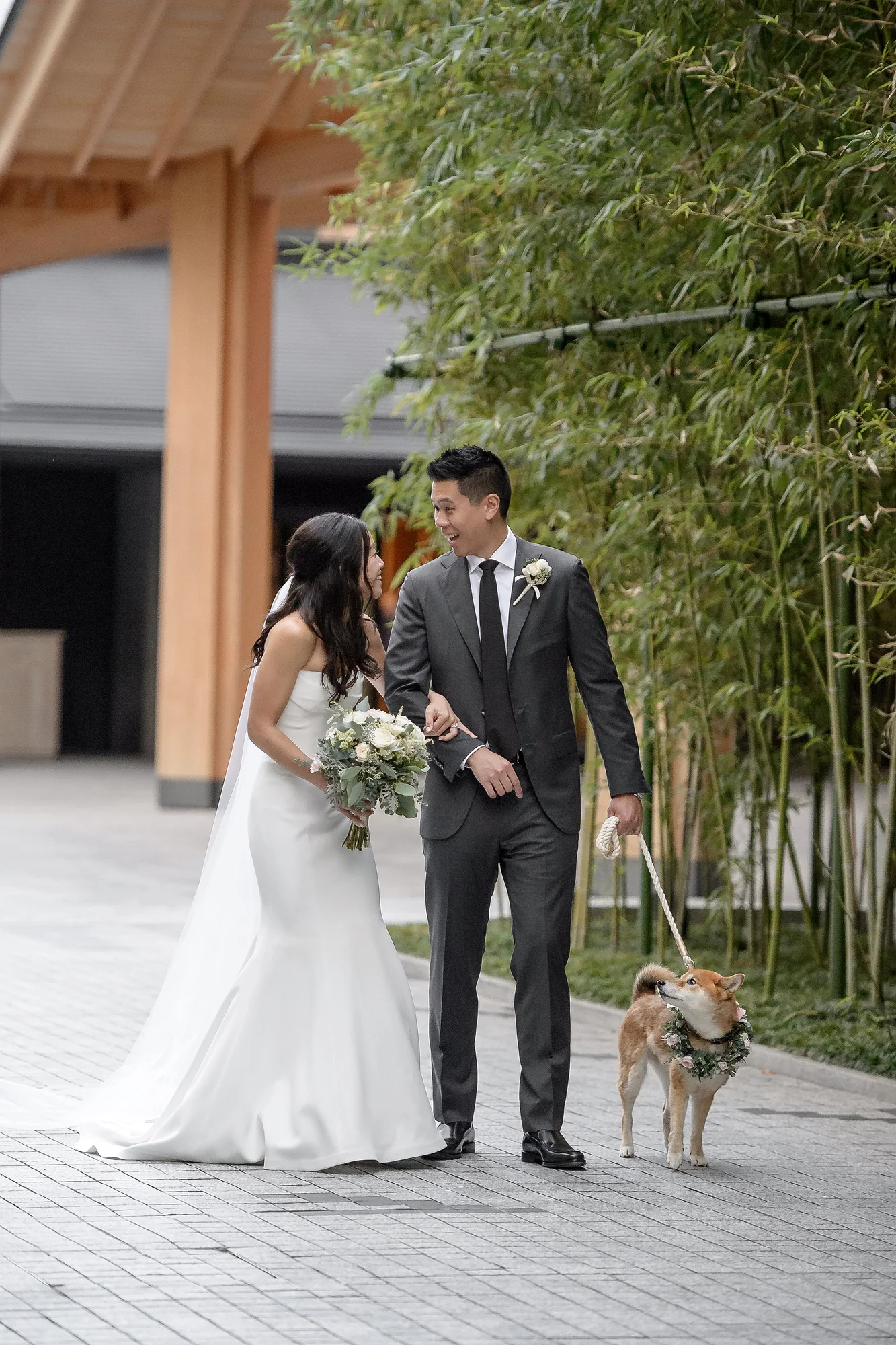 The couple stand in a stone courtyard edged with bamboo, their Shiba Inu on a lead beside them, in Kyoto.