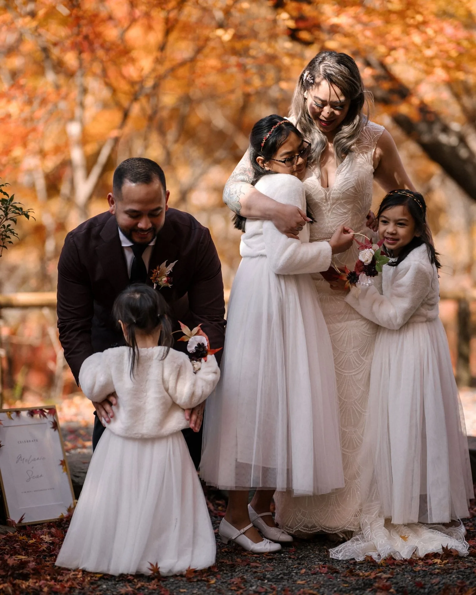 The couple hug their daughters in white dresses beneath the maples in Kyoto.