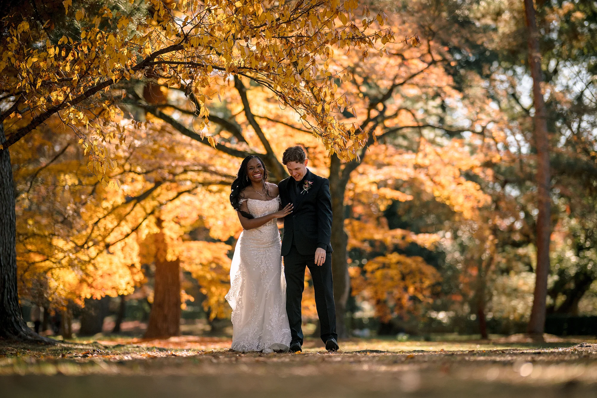 The couple walk laughing beneath golden autumn trees in a Kyoto park.