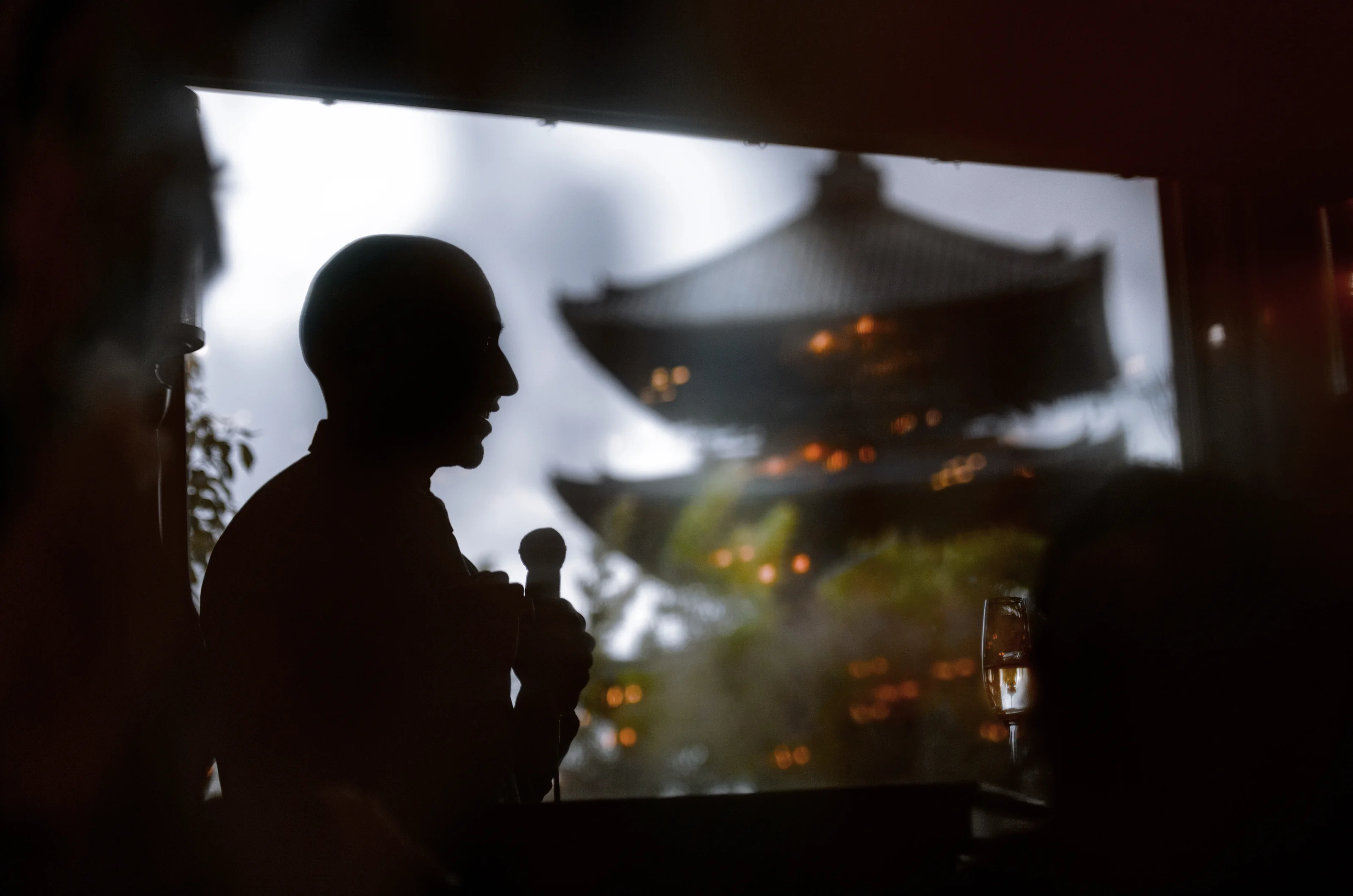 A guest gives a speech in silhouette against a window framing a lit pagoda in Kyoto.
