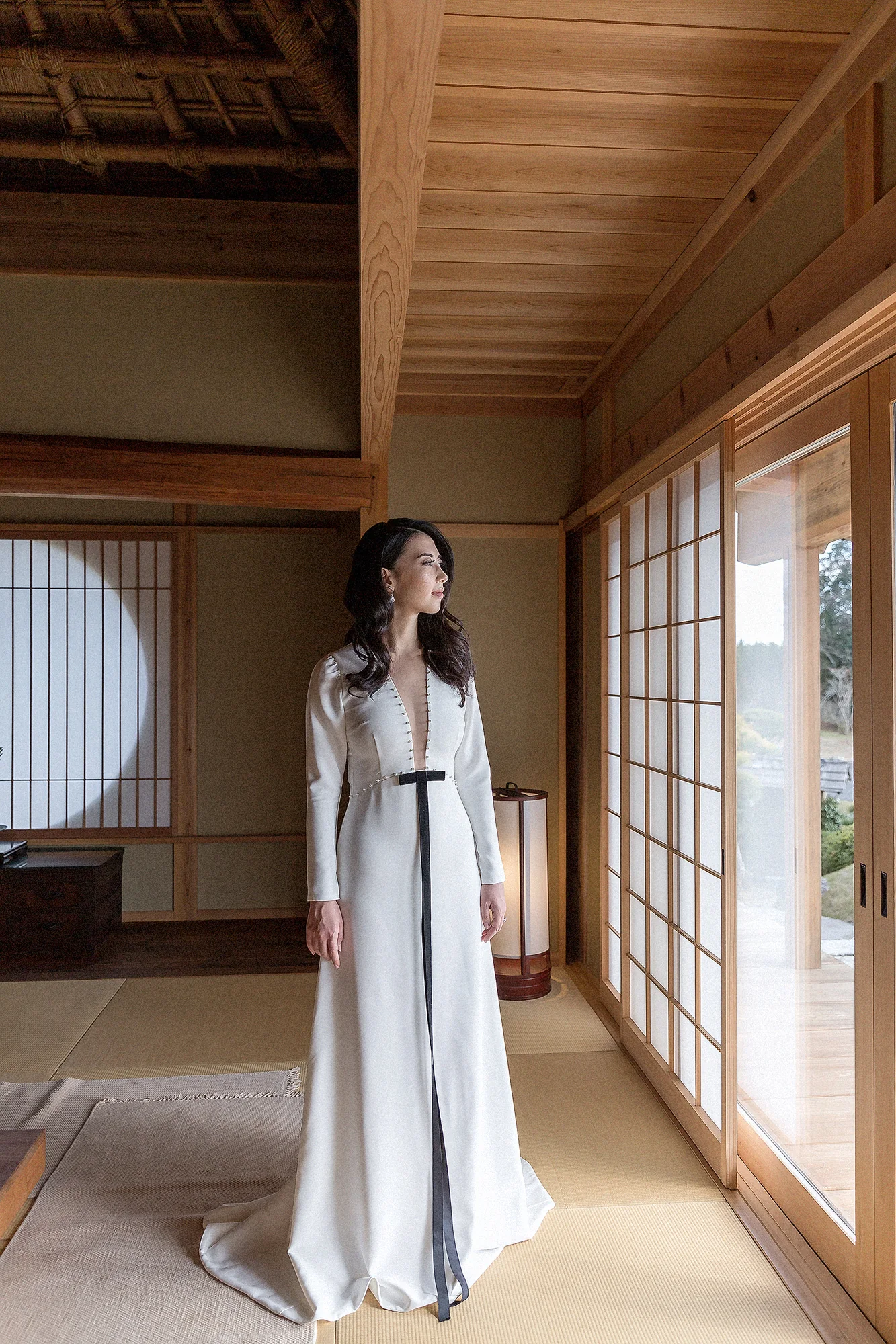 The bride stands in a tatami corridor lined with shoji and round windows in Kyoto.