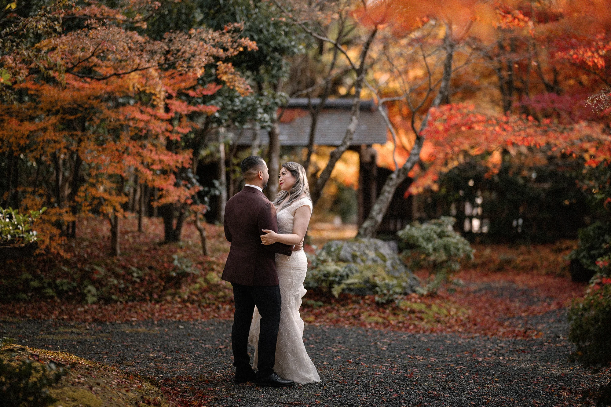 Couple embracing beneath red and orange maple leaves in Kyoto.