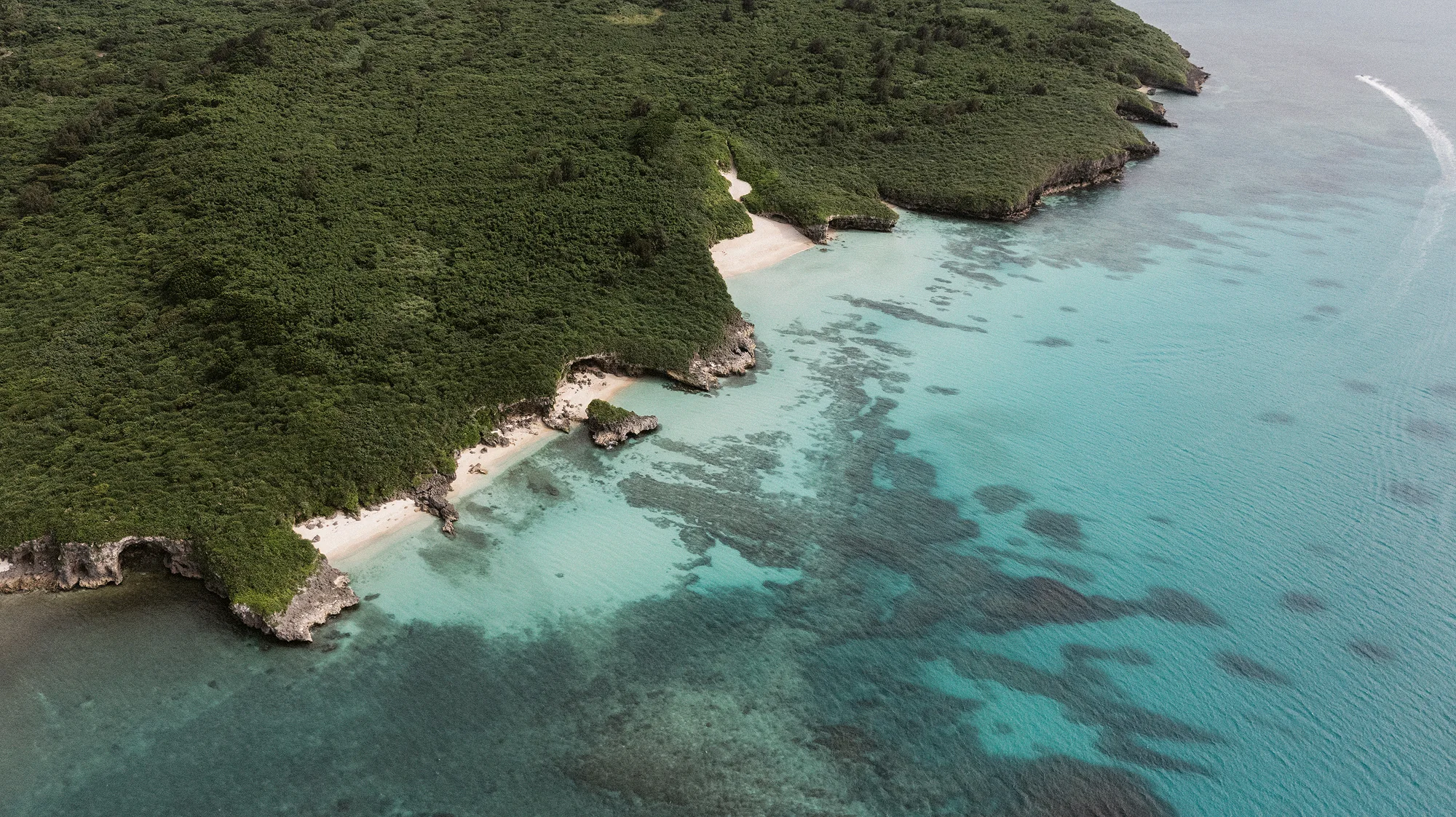 From above, a green headland meets reef and turquoise water off Miyakojima.