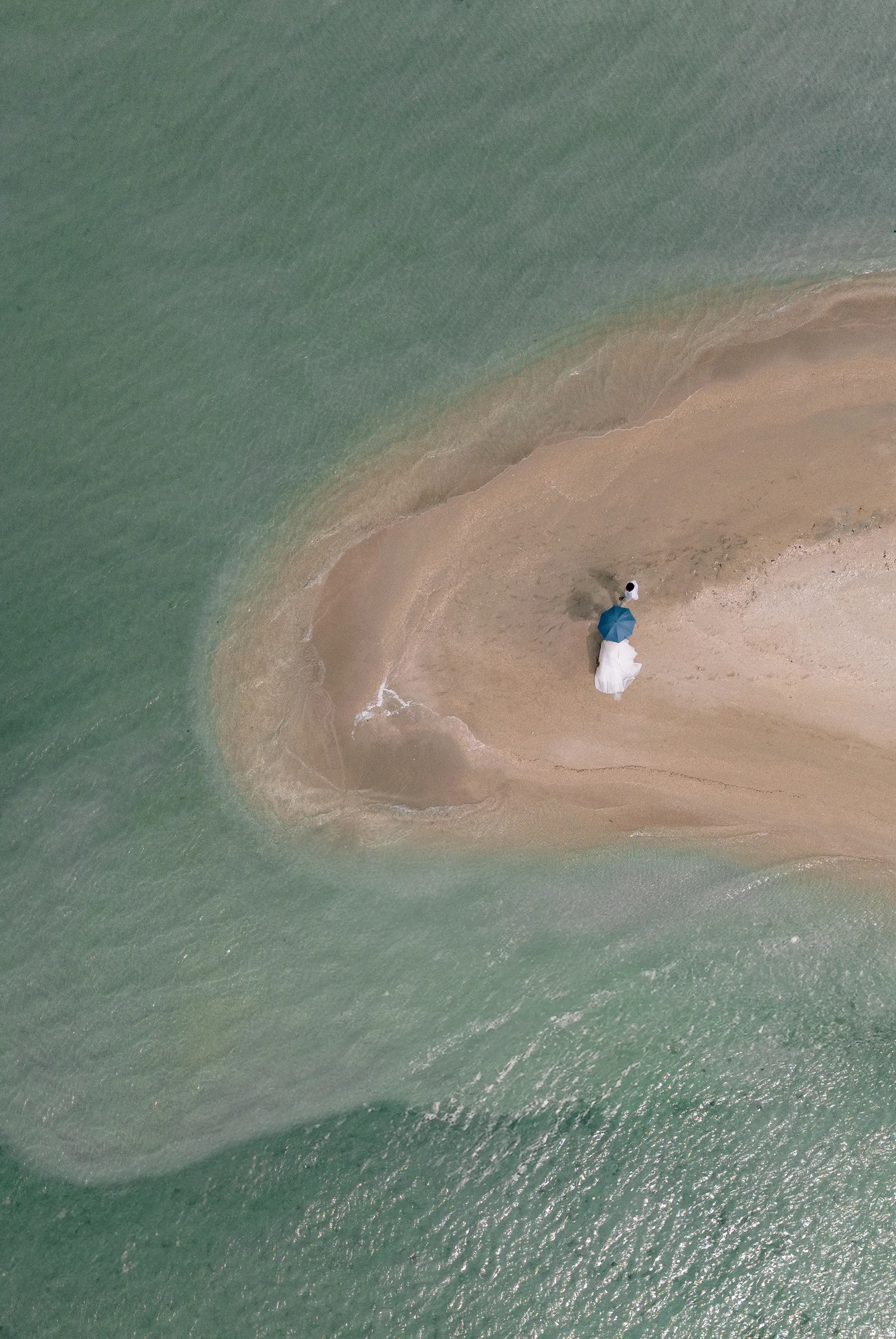 From above, a white sand spit curls into turquoise shallows off Miyakojima, the couple small at its tip.