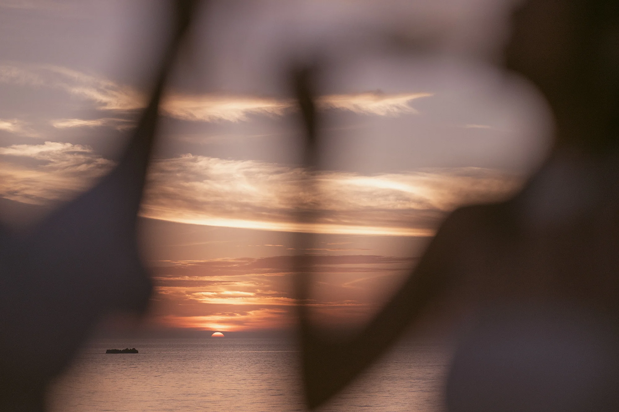 The sun sets over the sea through a soft dark sweep of the bride's hair in Miyakojima.