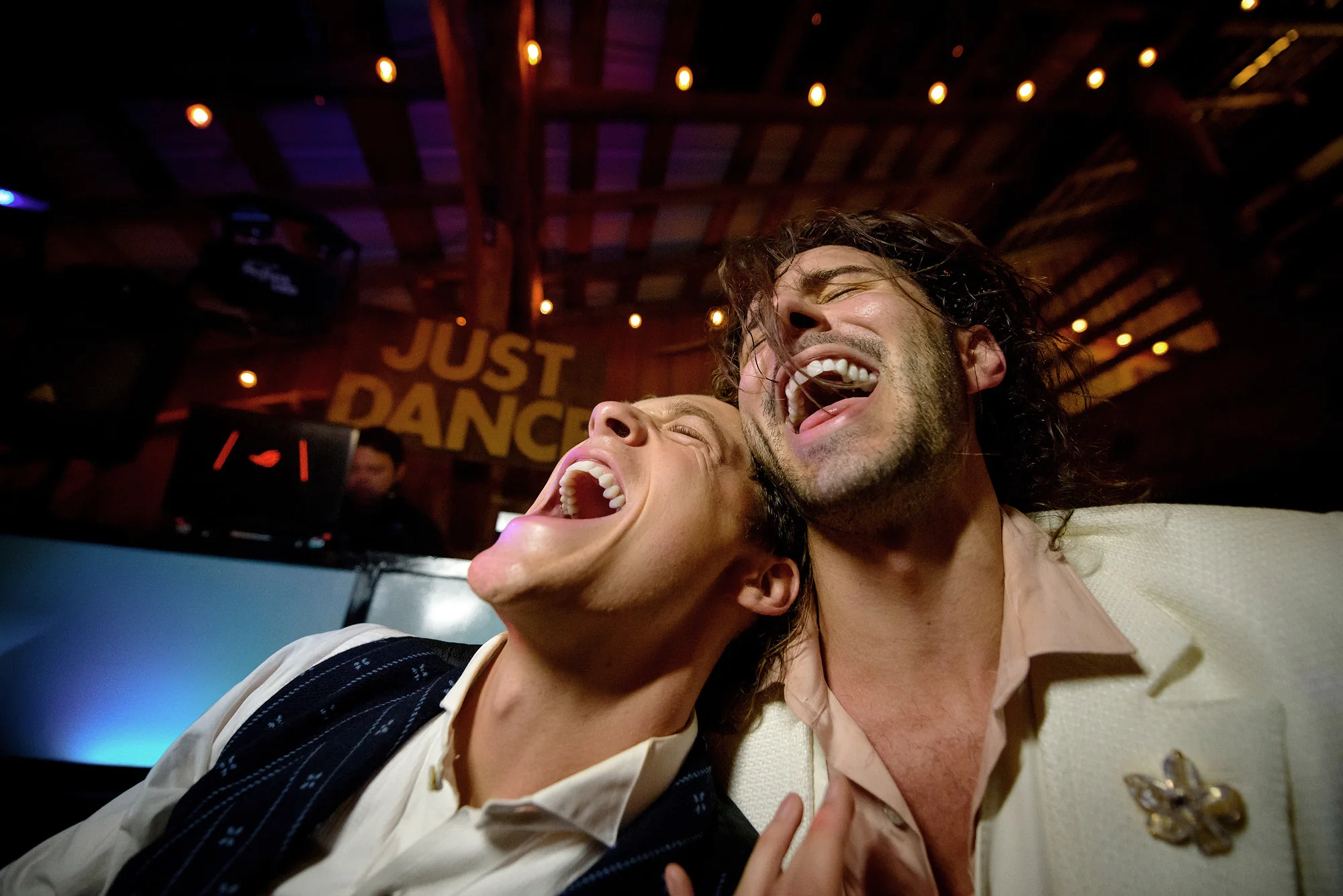 Two grooms laugh together under colored lights on the dance floor in Montana.